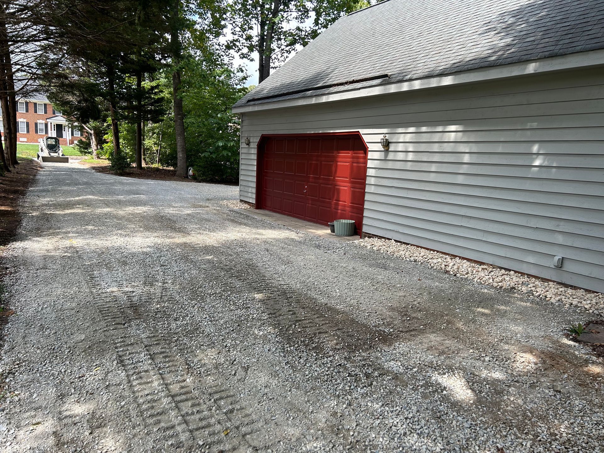 A garage with a red door is next to a gravel driveway.