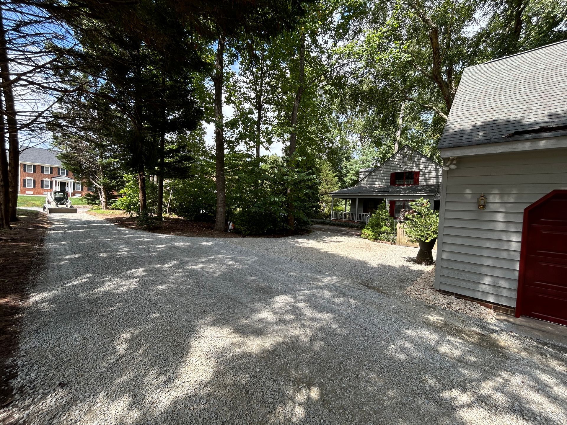 A gravel driveway leading to a garage and a house surrounded by trees.