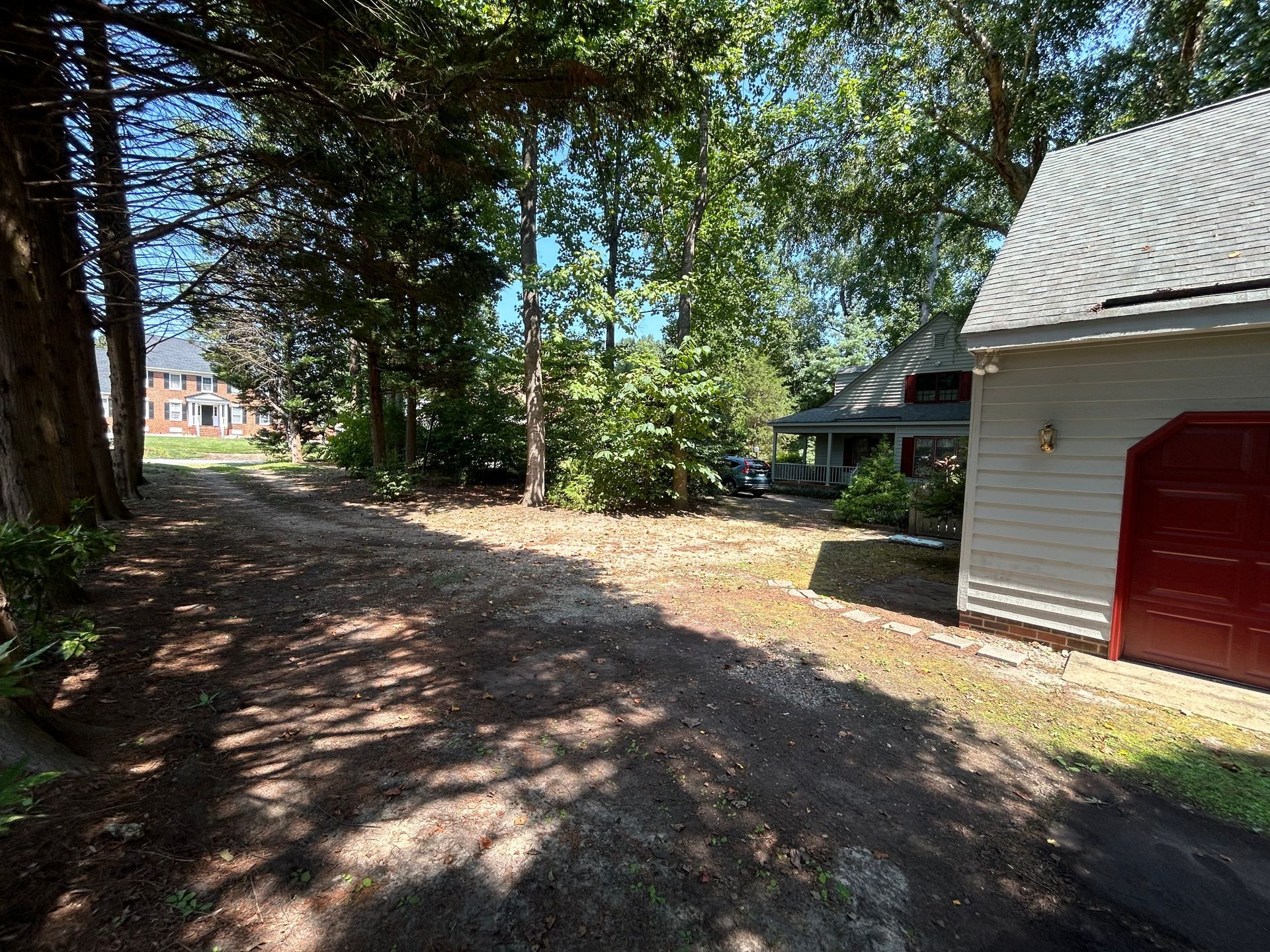 A dirt road leading to a house with a red garage door.