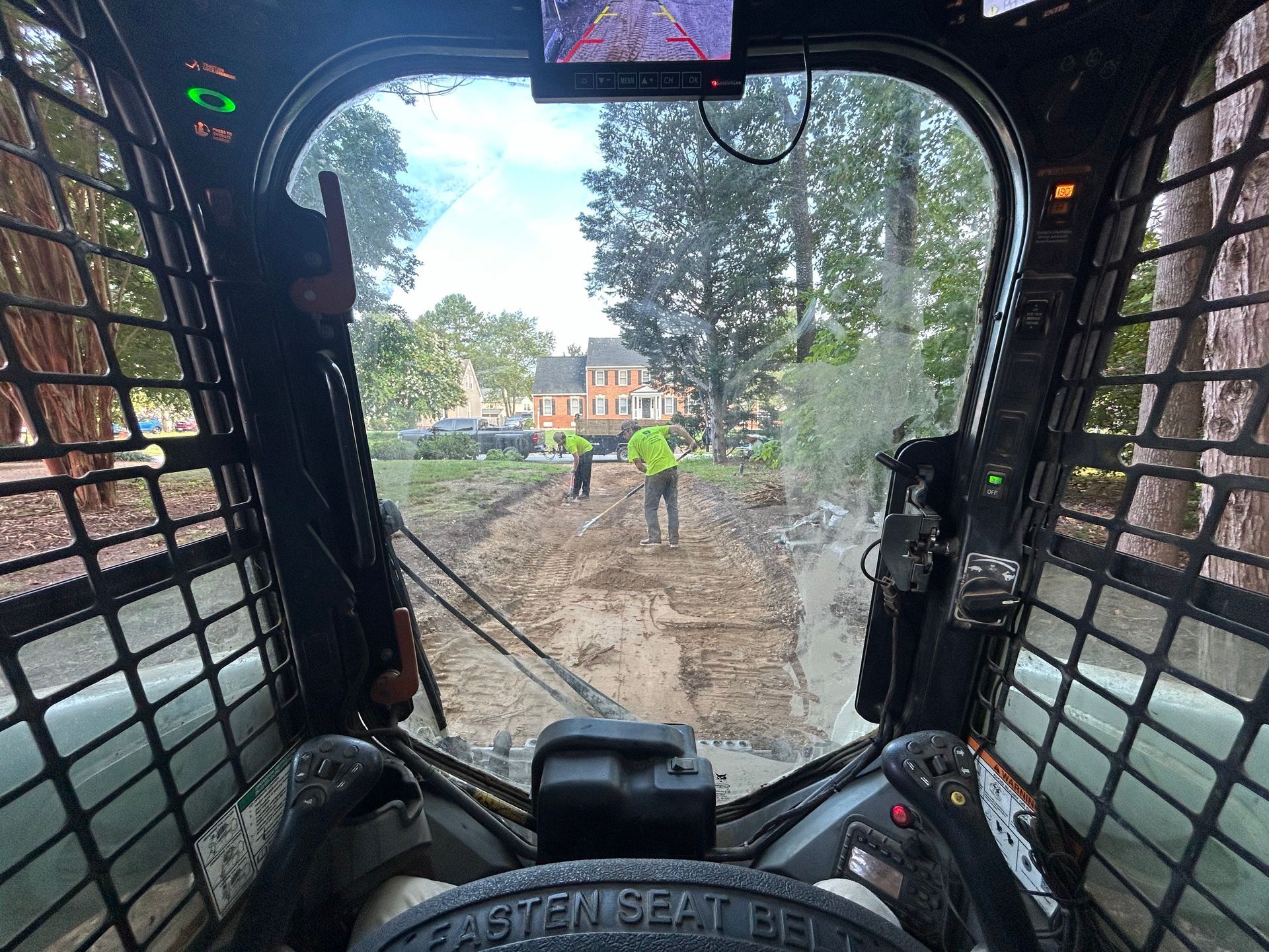A person is driving a skid steer on a dirt road.