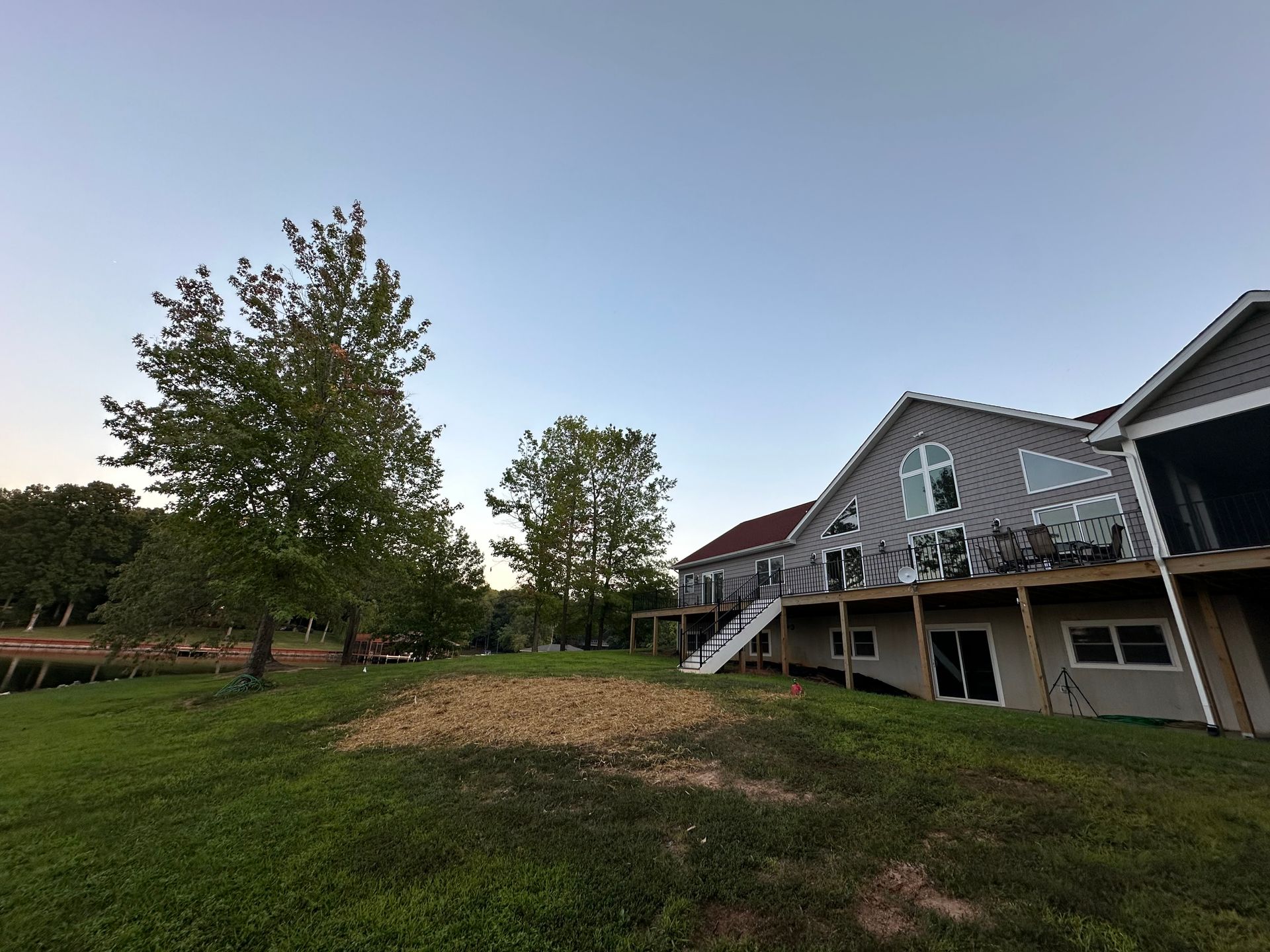 A large house with a large deck is sitting on top of a lush green field.