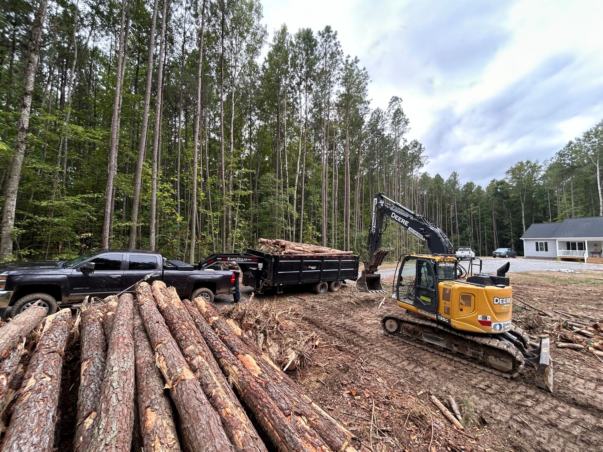 A bulldozer is moving logs in a pile in the middle of a forest.