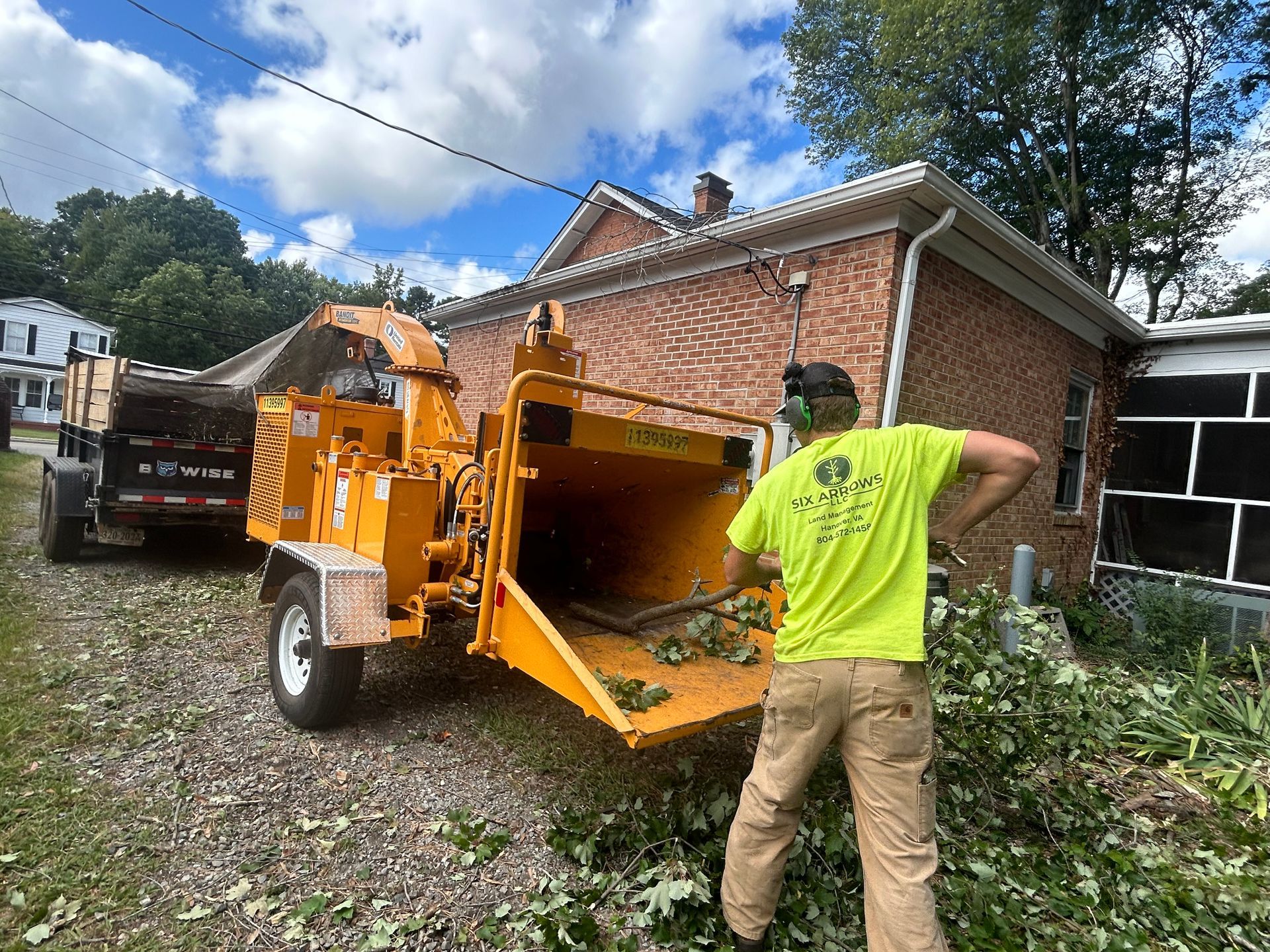 A man is standing next to a tree chipper in front of a brick house.