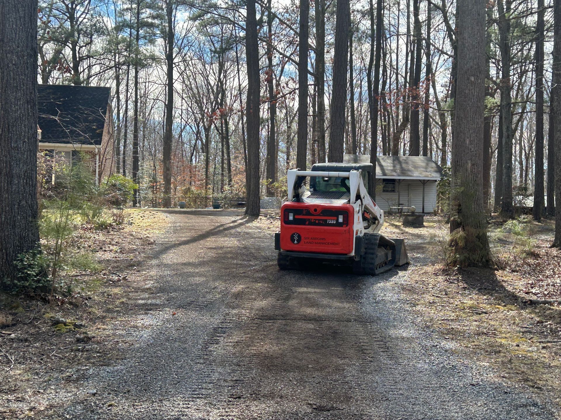 A bobcat is driving down a dirt road in the woods.