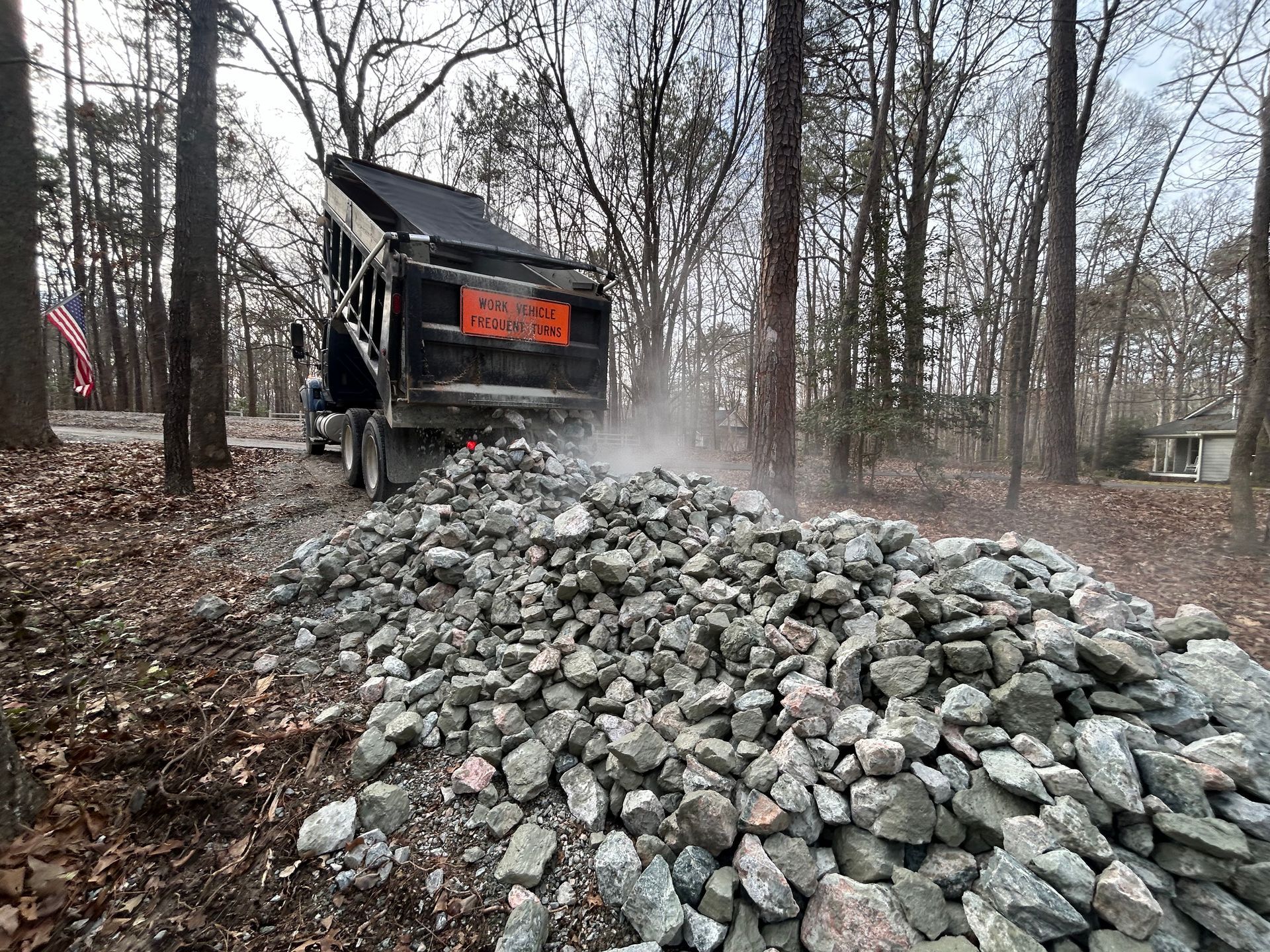 A dump truck is loading rocks into a pile in the woods.