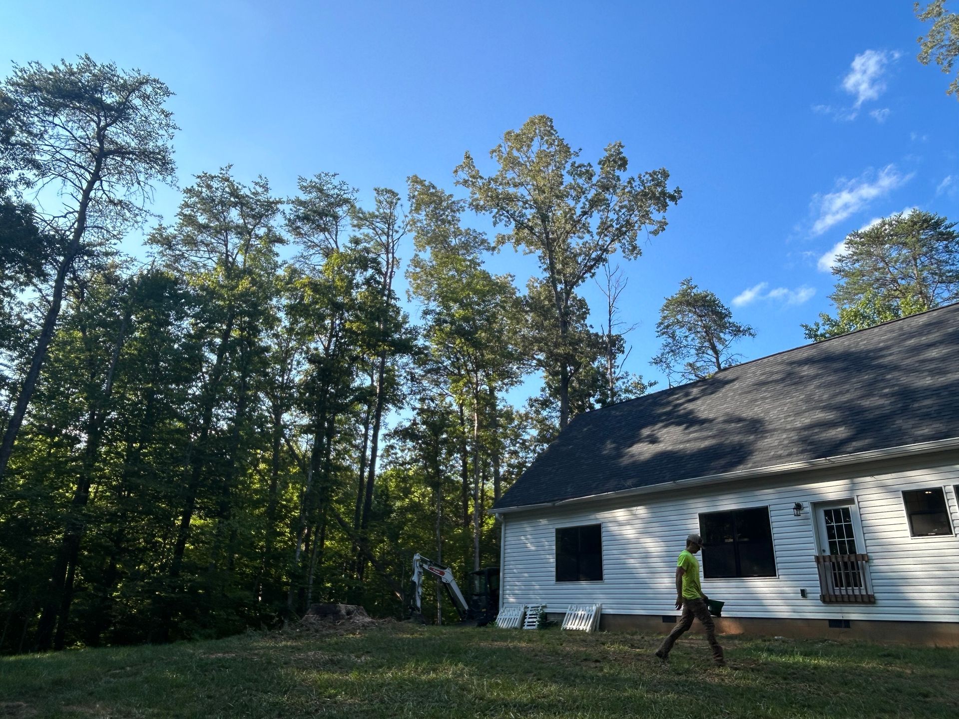 A person walking in front of a white house with trees in the background