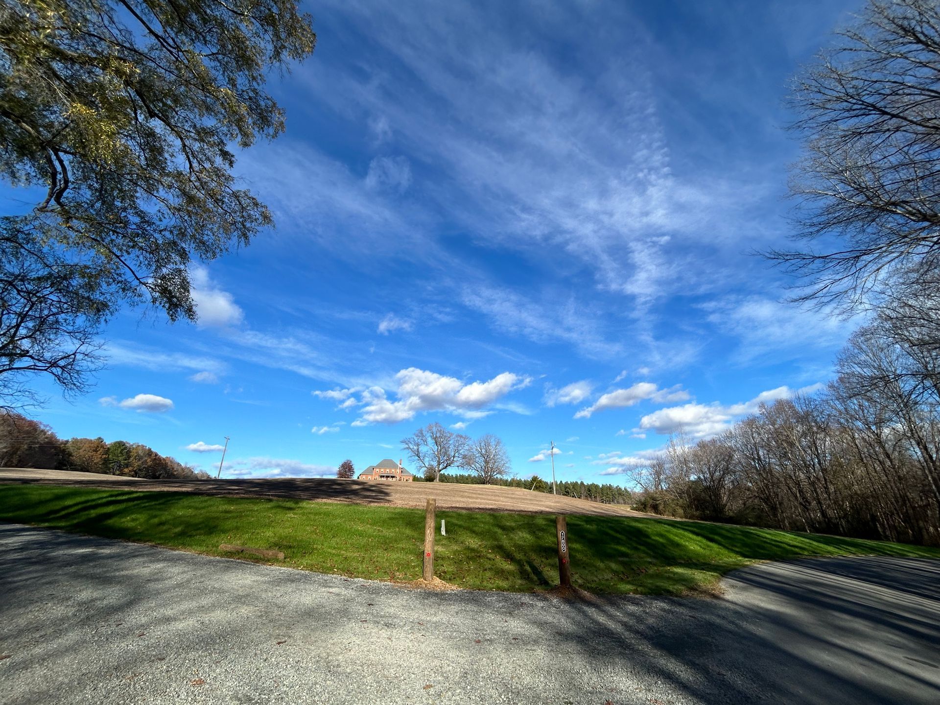 A dirt road going through a grassy field with a blue sky and clouds.