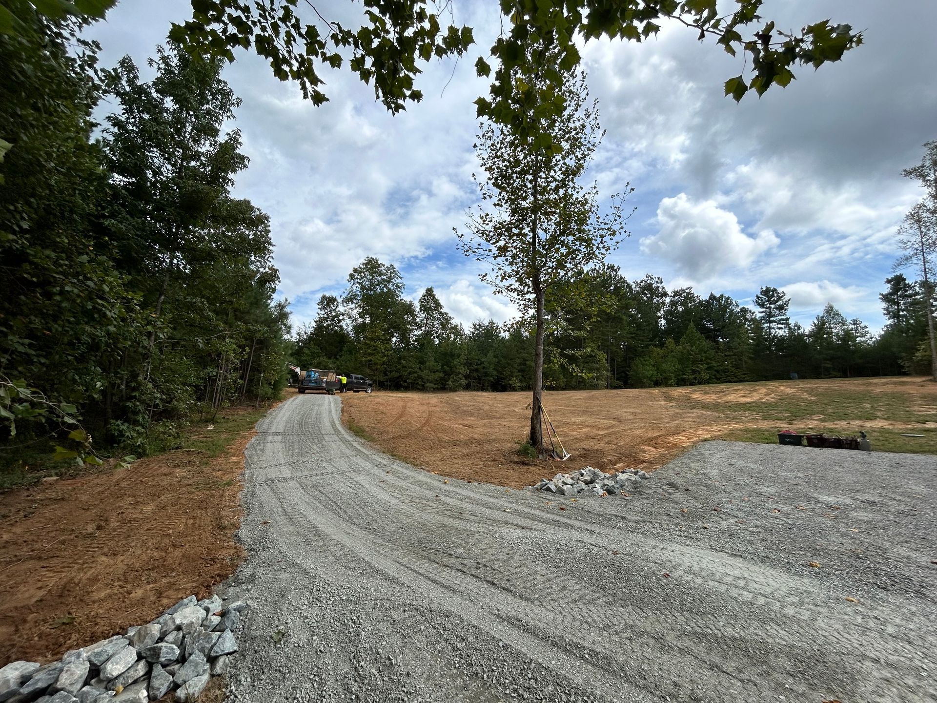 A gravel road going through a field with trees on both sides.