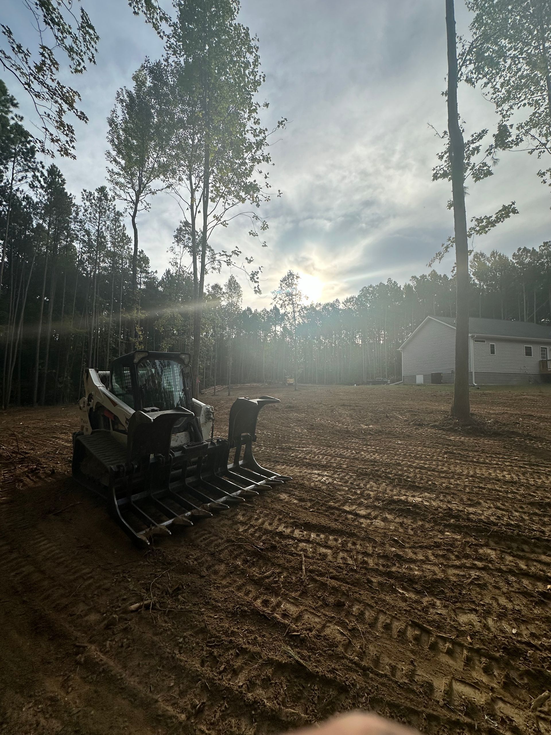 A bulldozer is driving through a dirt field with trees in the background.