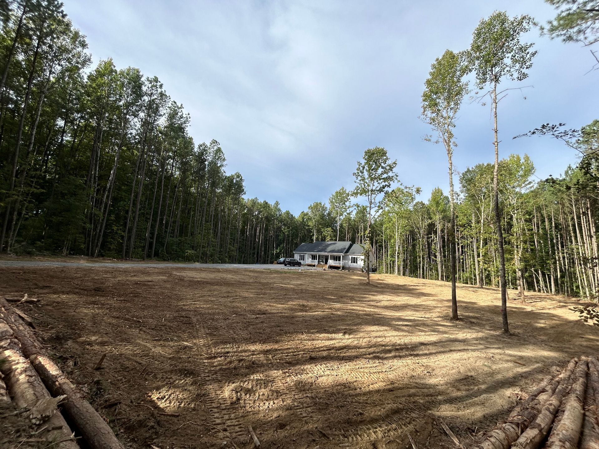 A house is sitting in the middle of a dirt field surrounded by trees.