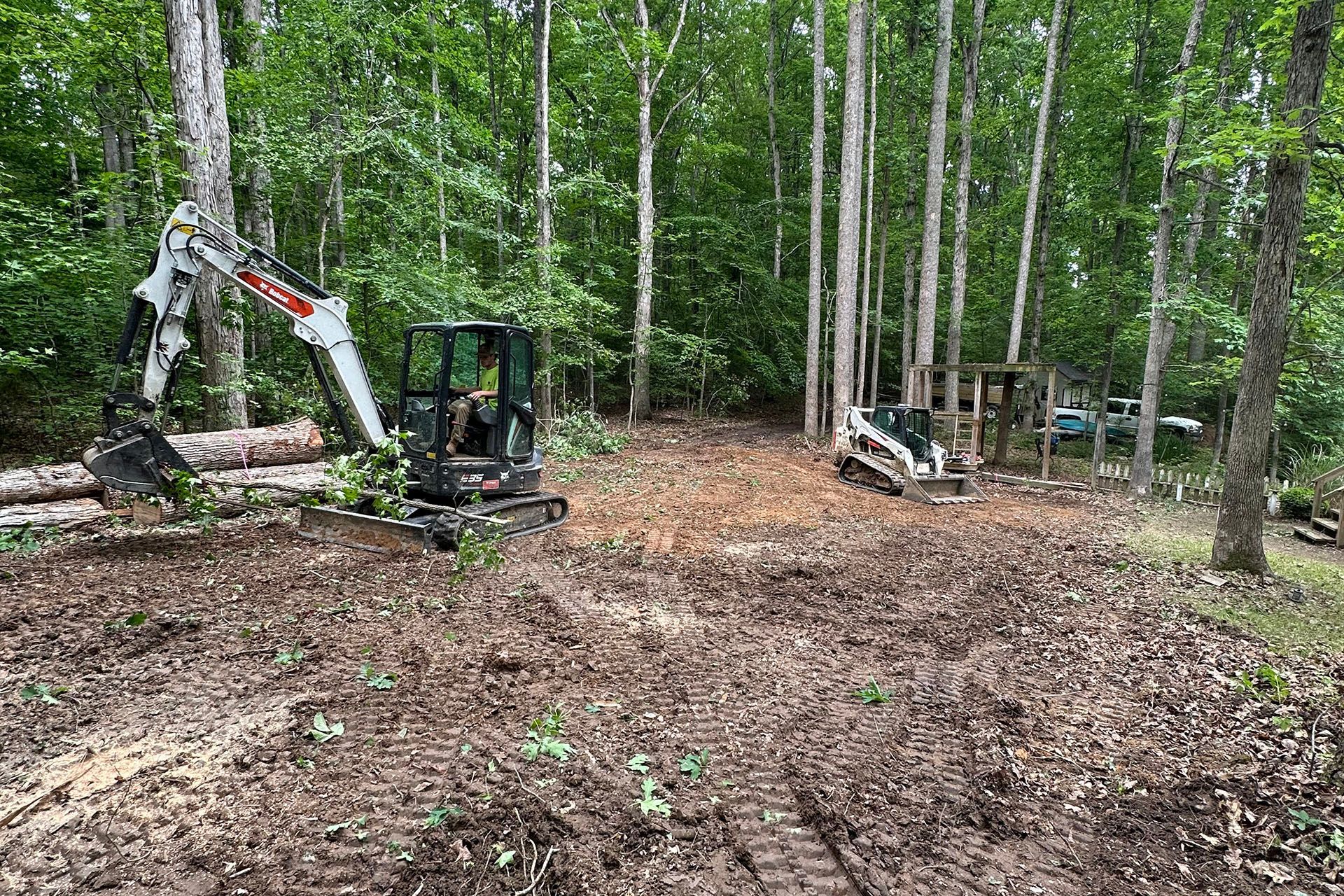 A small excavator is sitting in the middle of a forest.