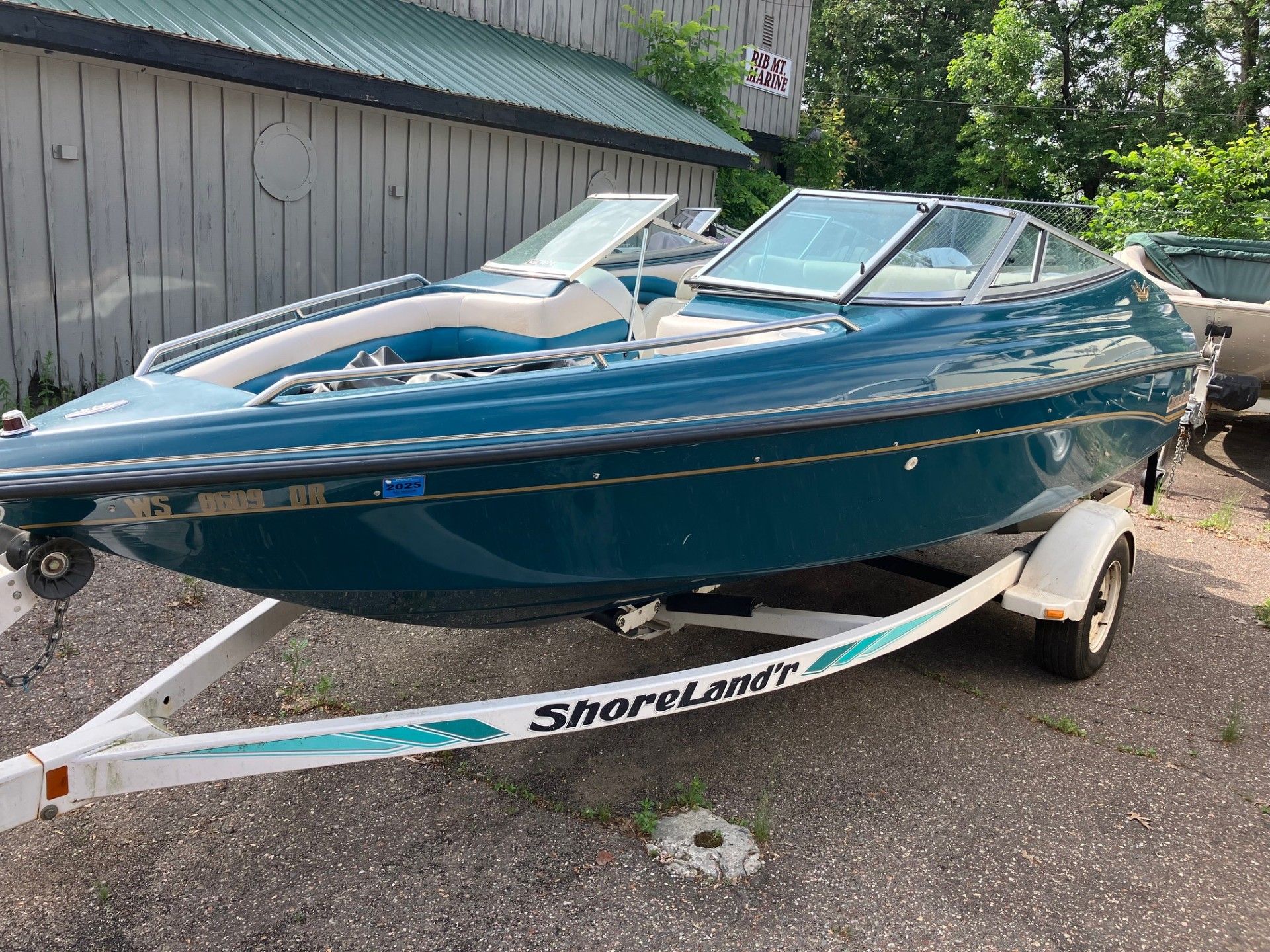 A blue boat is parked on a trailer in front of a building.
