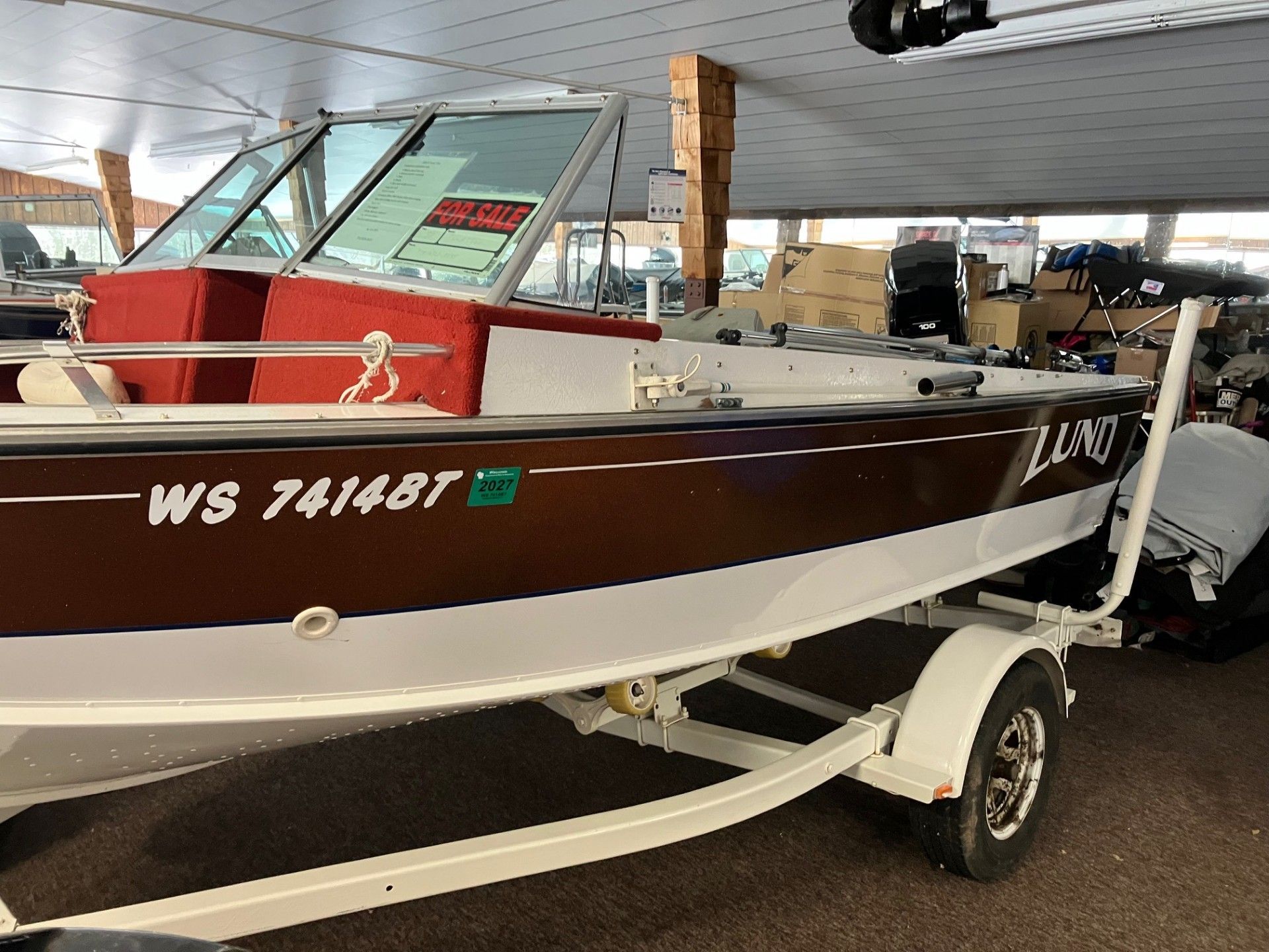 A brown and white Lund fishing boat on a trailer parked in a covered storage area. 