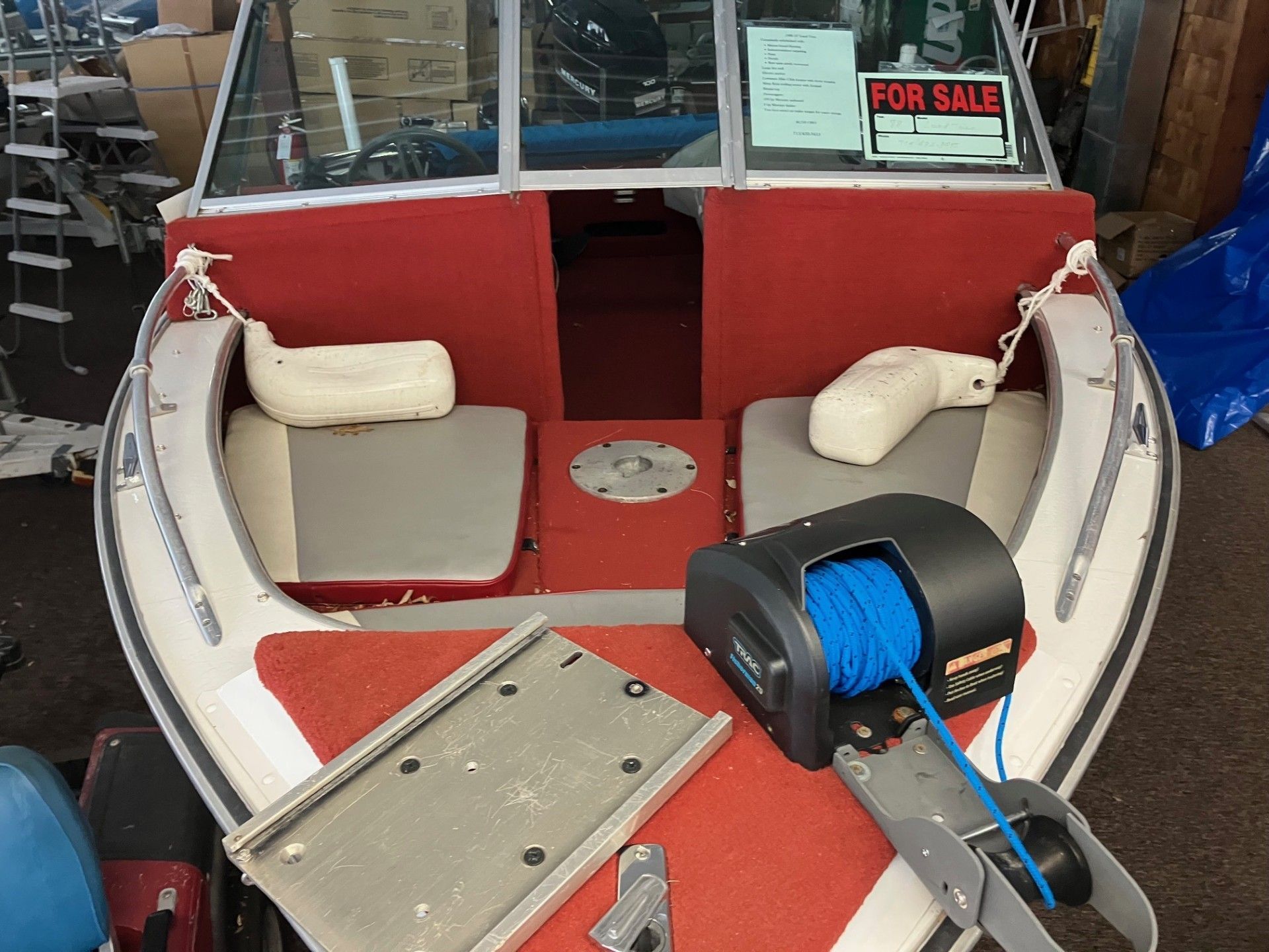A front-facing view of an open-bow boat interior with red carpet, gray seating, and a mounted blue rope winch. 