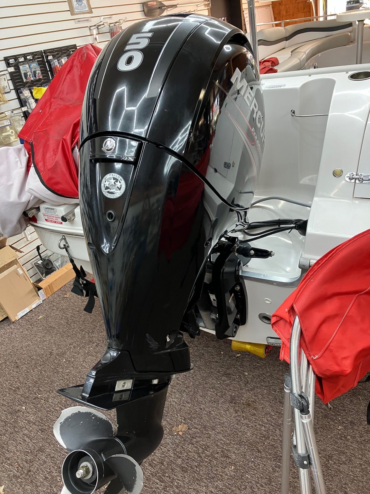 Black outboard motor mounted on a white boat, seen from the stern inside a workshop or garage.