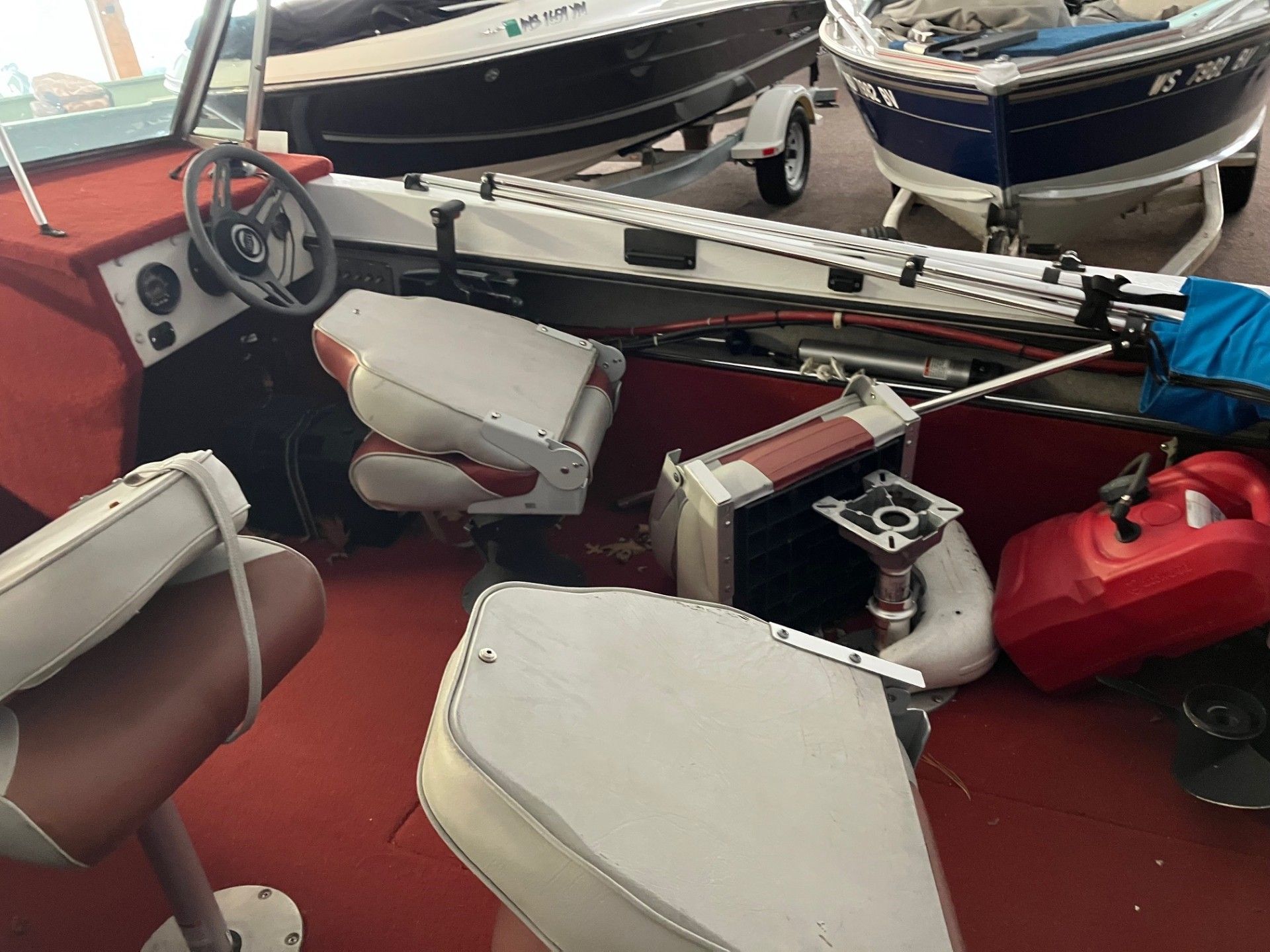 The interior of a boat showing a steering wheel, red carpeting, several gray seats, and a red portable fuel tank. 