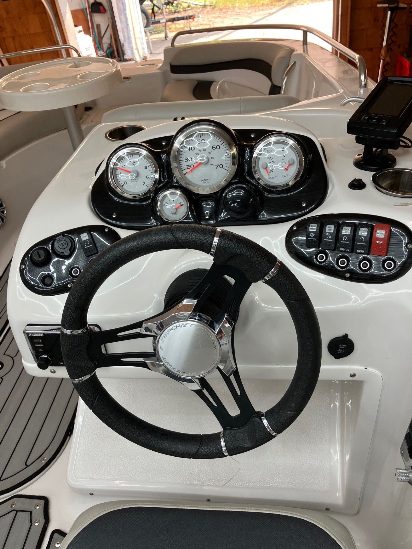 Boat helm with steering wheel, gauges, and control switches in a white dashboard console.