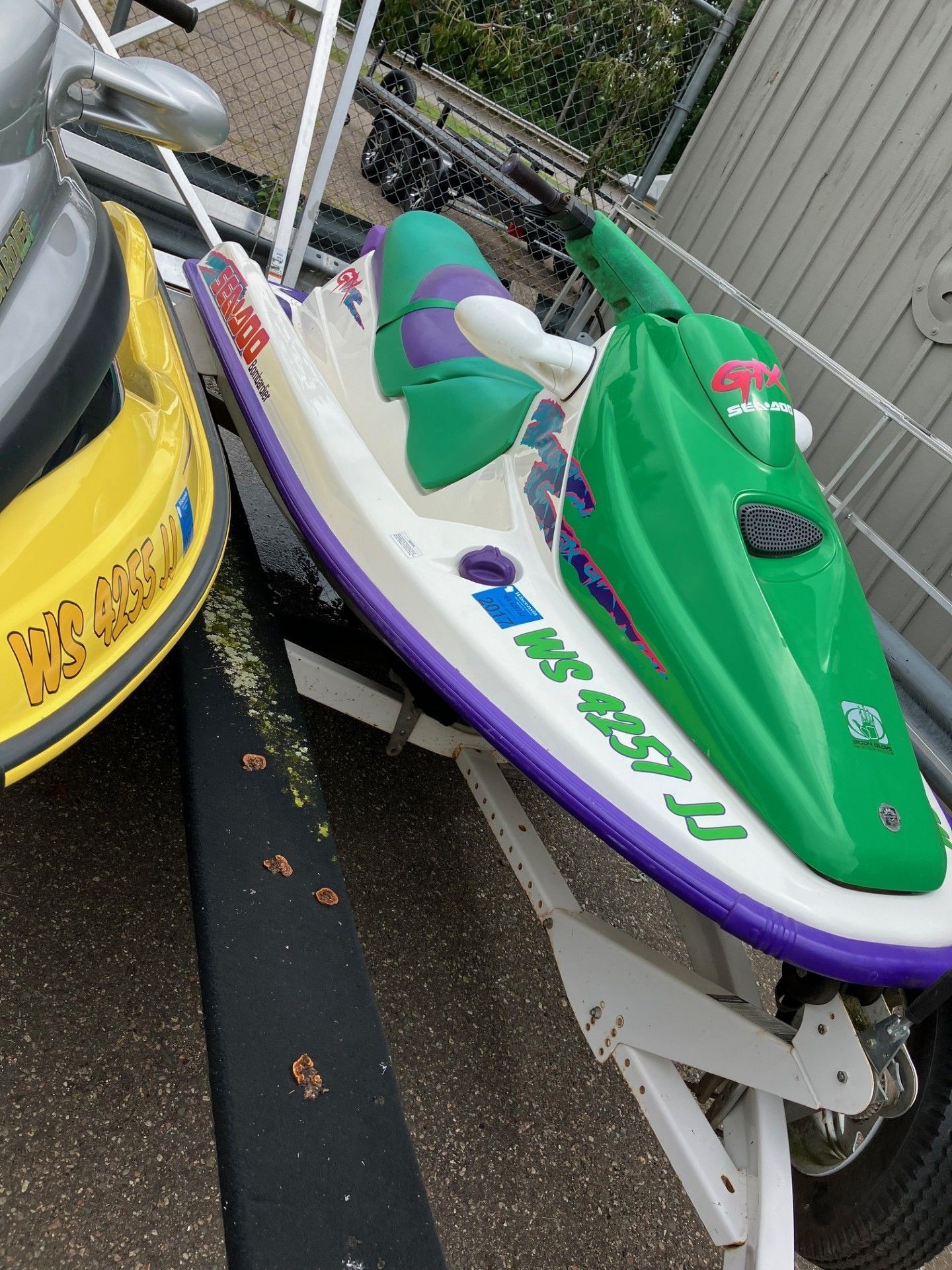 A green and white personal watercraft parked on a trailer next to a yellow watercraft. 
