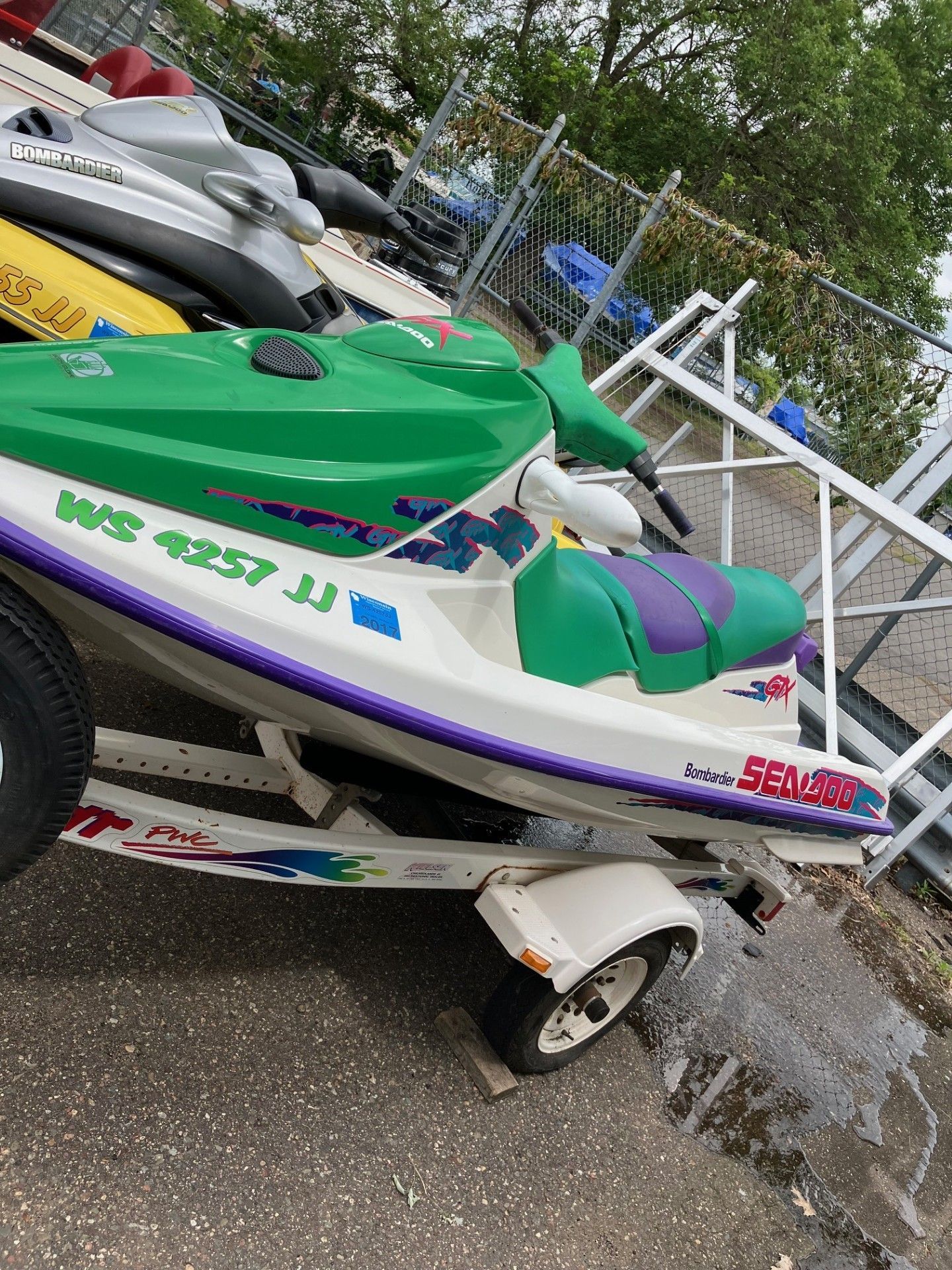 A green and white Sea-Doo personal watercraft sits on a trailer in an outdoor storage area next to another jet ski. 
