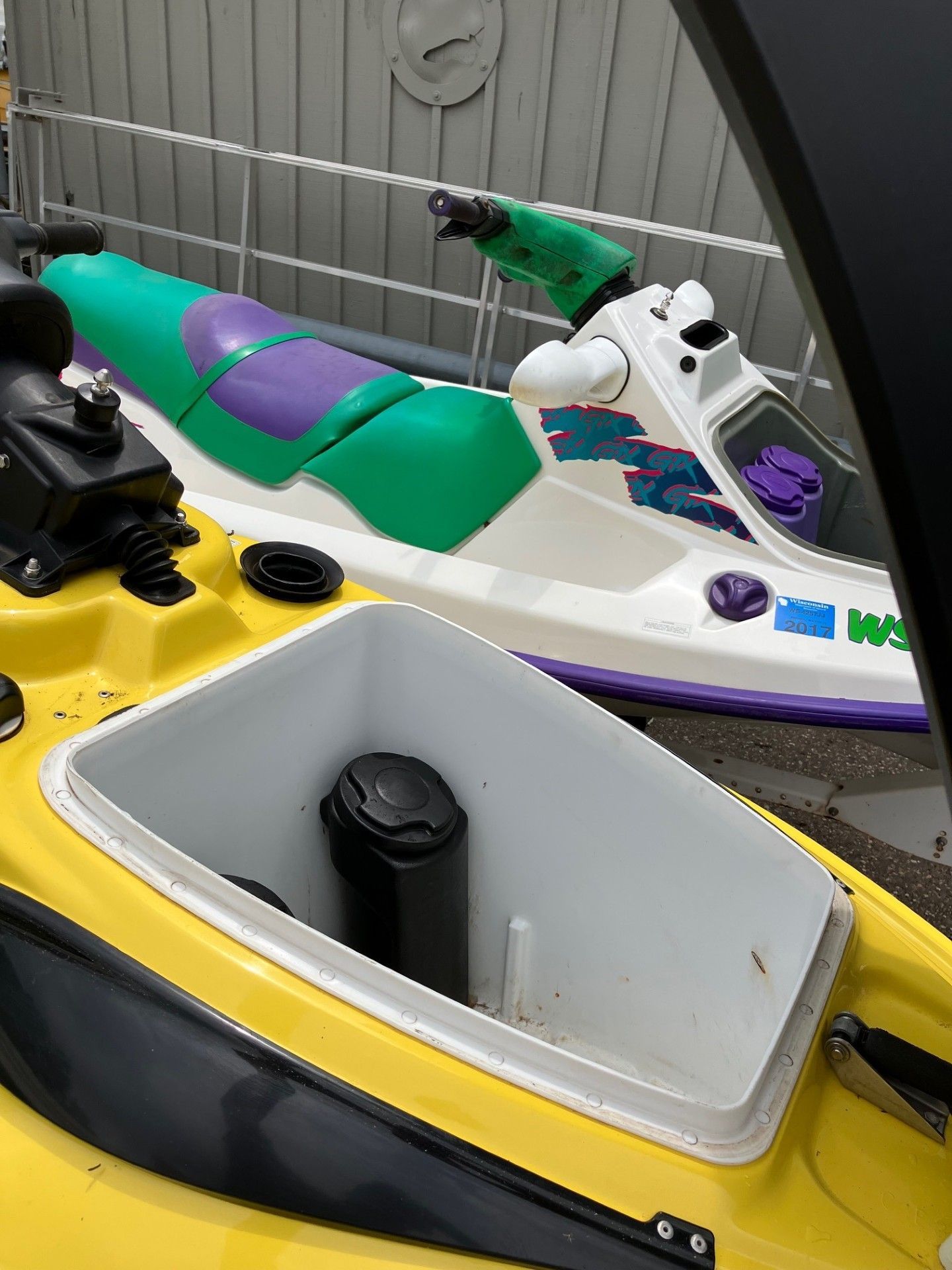 A high-angle view shows the front storage compartment of a yellow jet ski, with a green and purple jet ski in the back. 