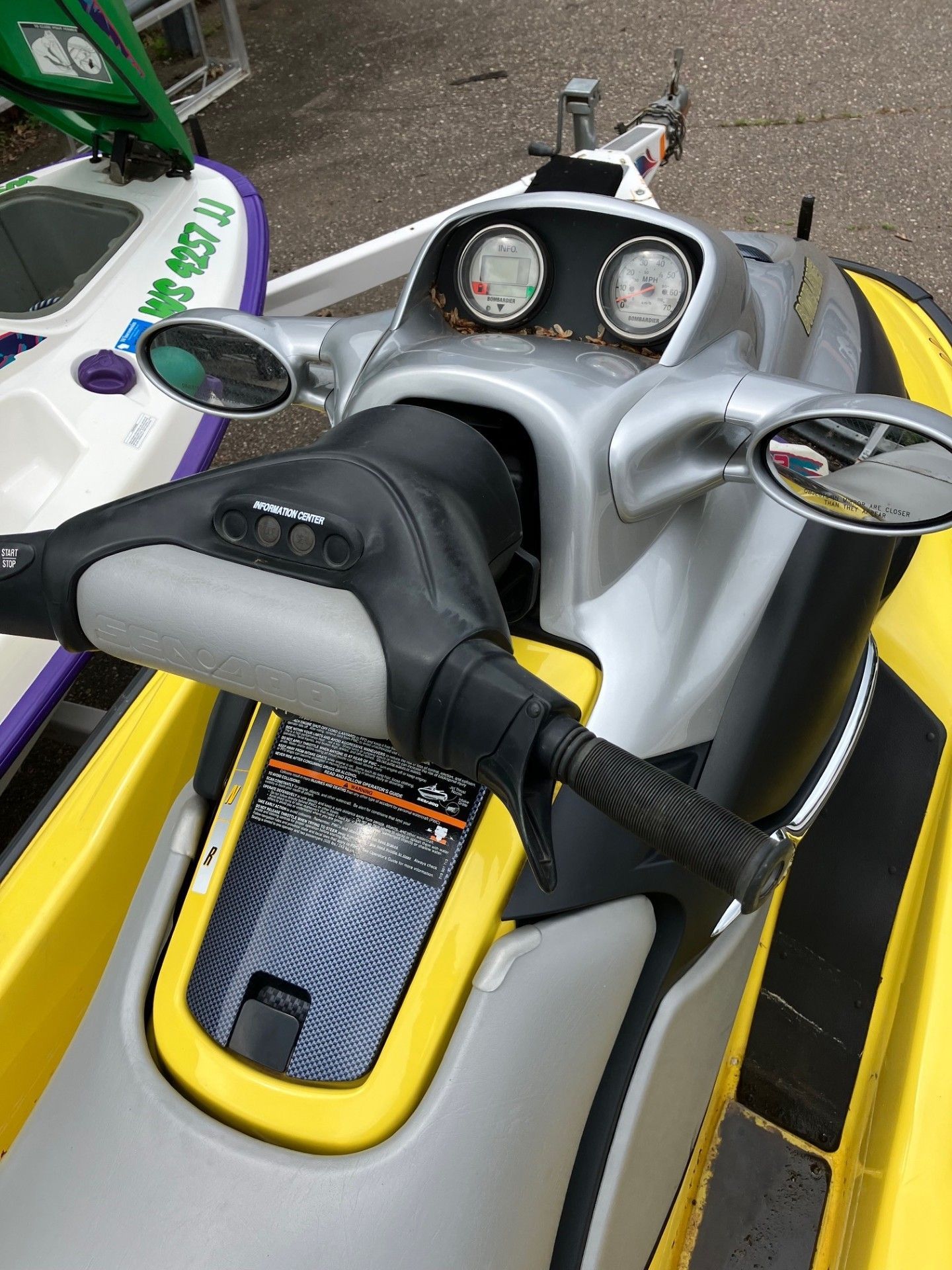 A close-up view of the handlebars, console, and mirrors of a yellow and silver personal watercraft on a trailer. 