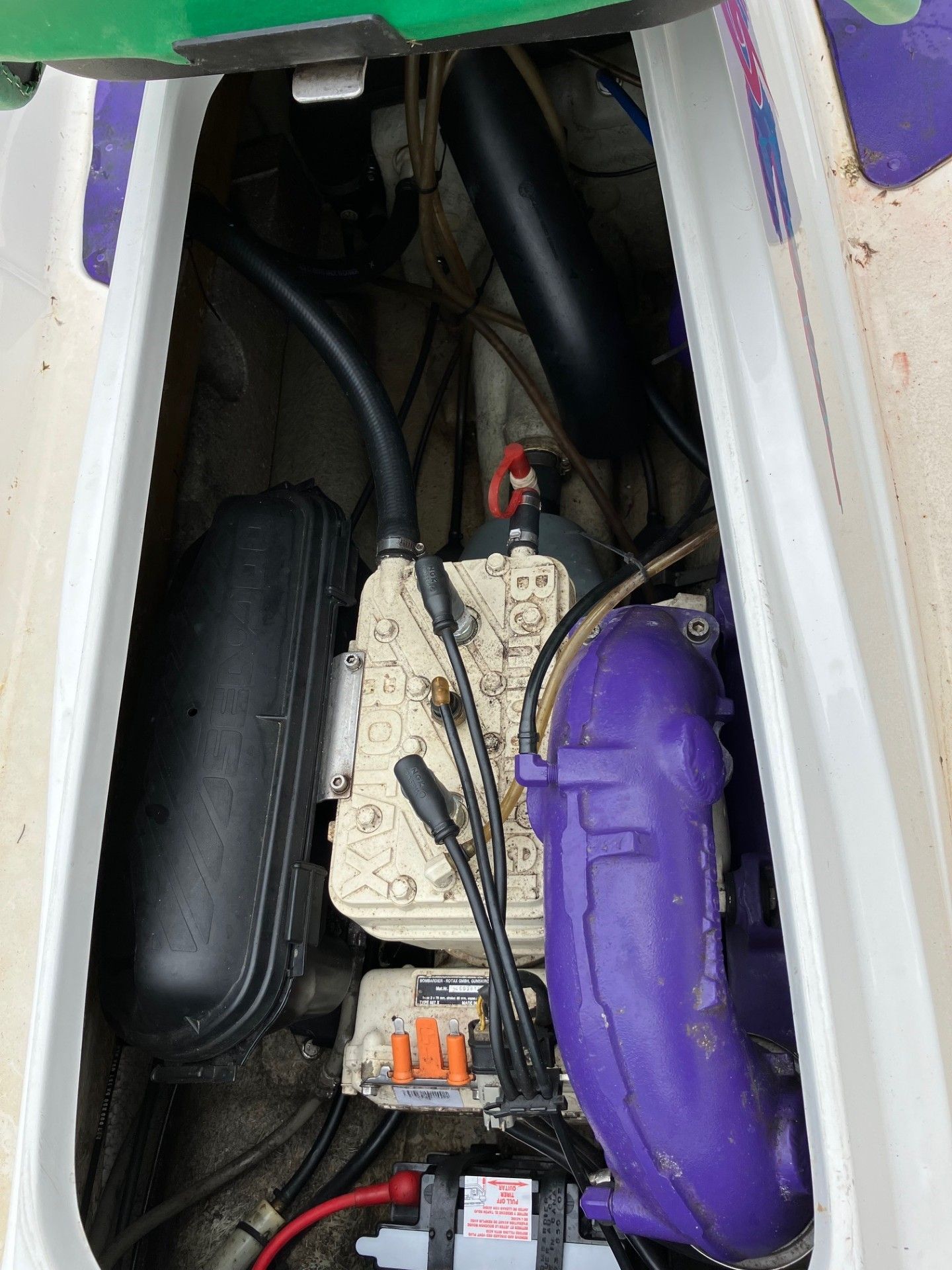 An overhead view of the open engine compartment of a personal watercraft featuring a tan engine and purple exhaust pipe. 