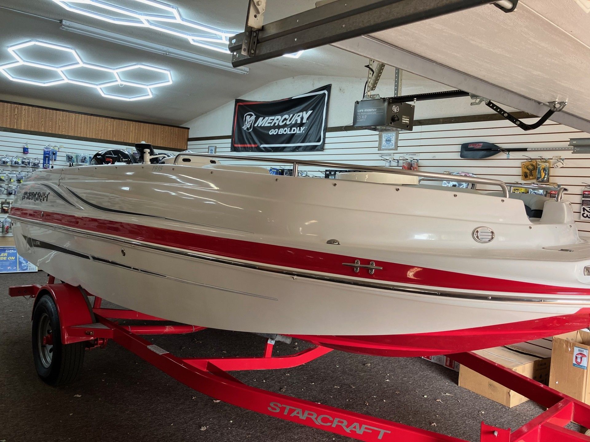 Beige and red boat on a trailer inside a showroom or garage with LED lights overhead