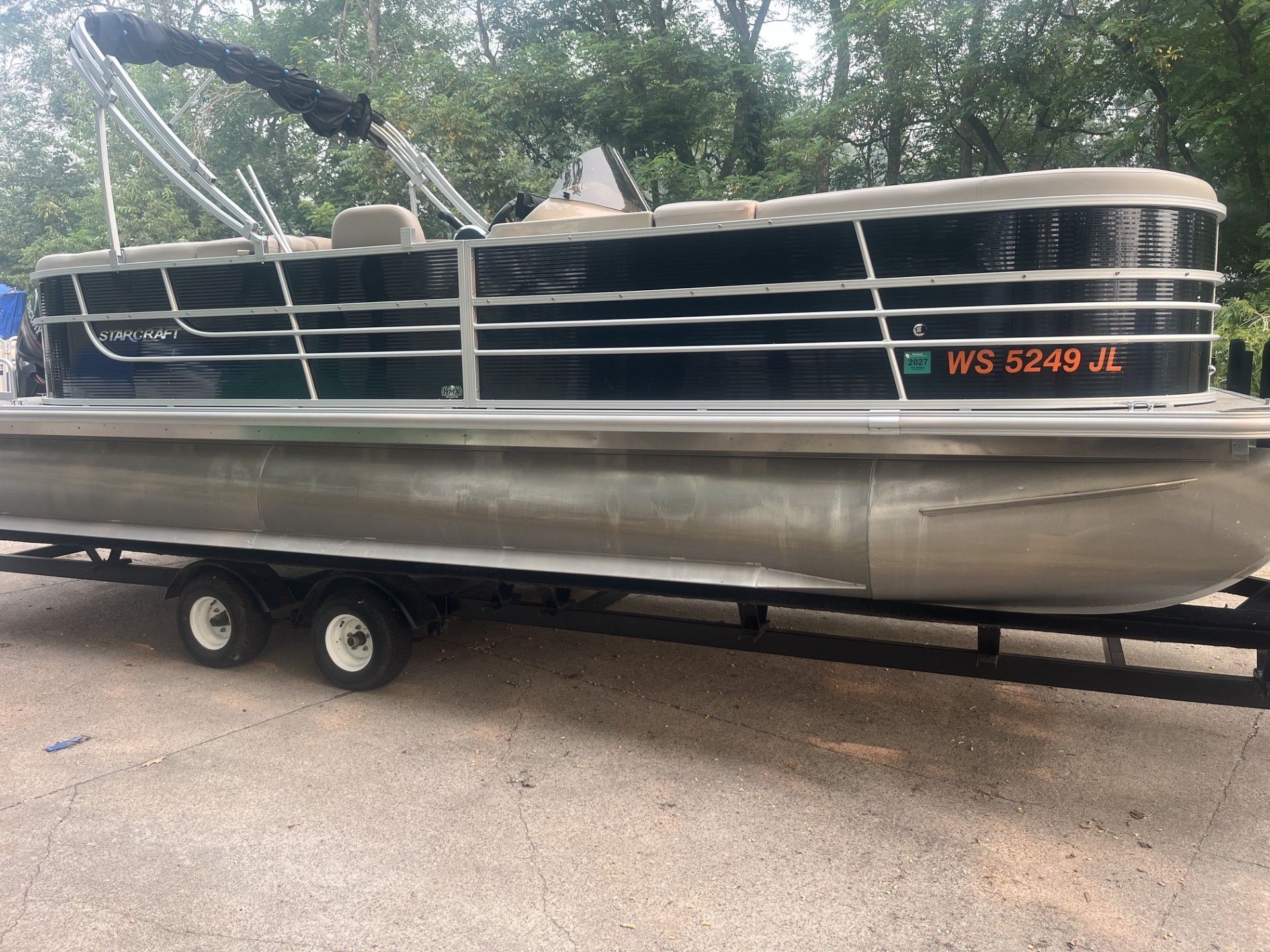 Starcraft 236 Party Lounger boat on a trailer parked outdoors, with black-and-silver railings and a tan seating cover