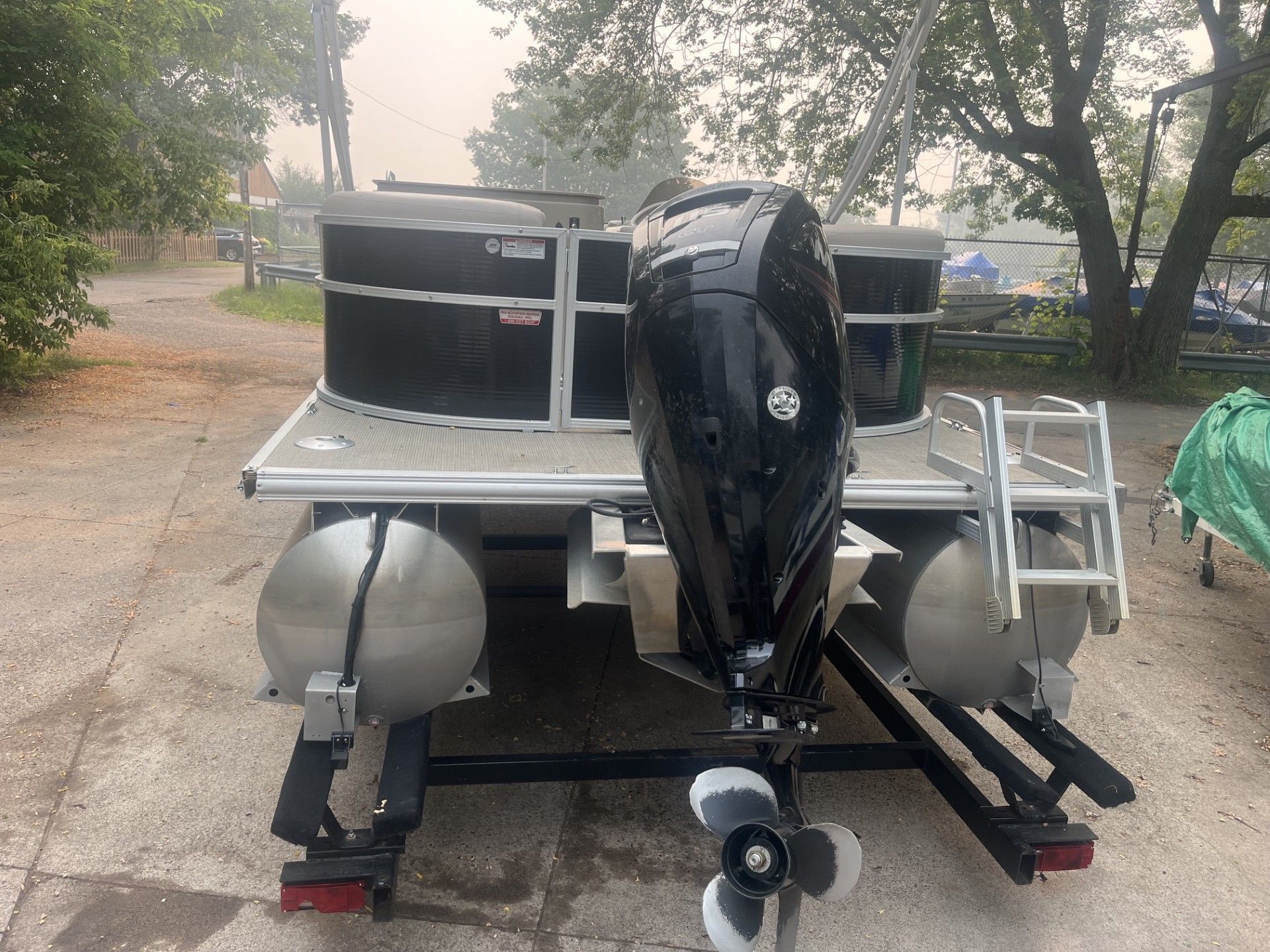 Starcraft 236 Party Lounger boat on a trailer, seen from behind on a tree-lined road.