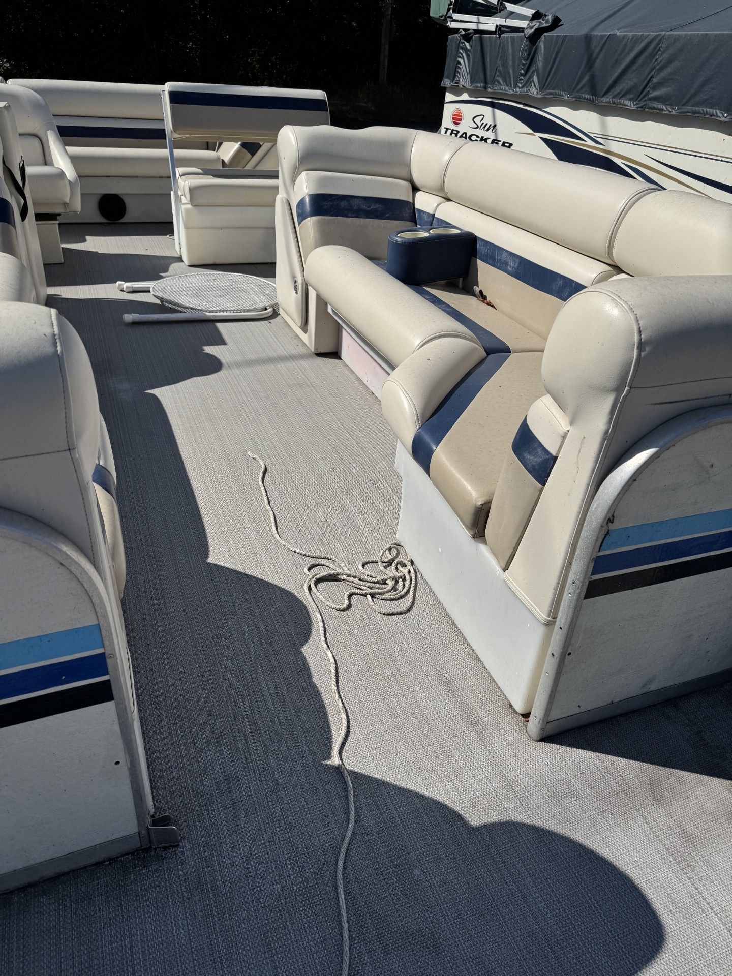 Boat deck with beige cushioned bench seating and gray carpeting in bright sunlight
