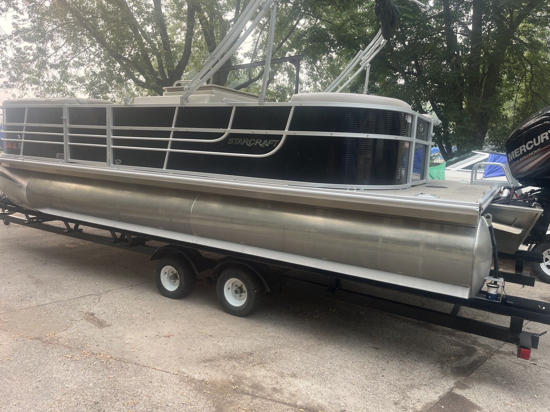 Starcraft 236 Party Lounger boat on a trailer parked on gravel under trees