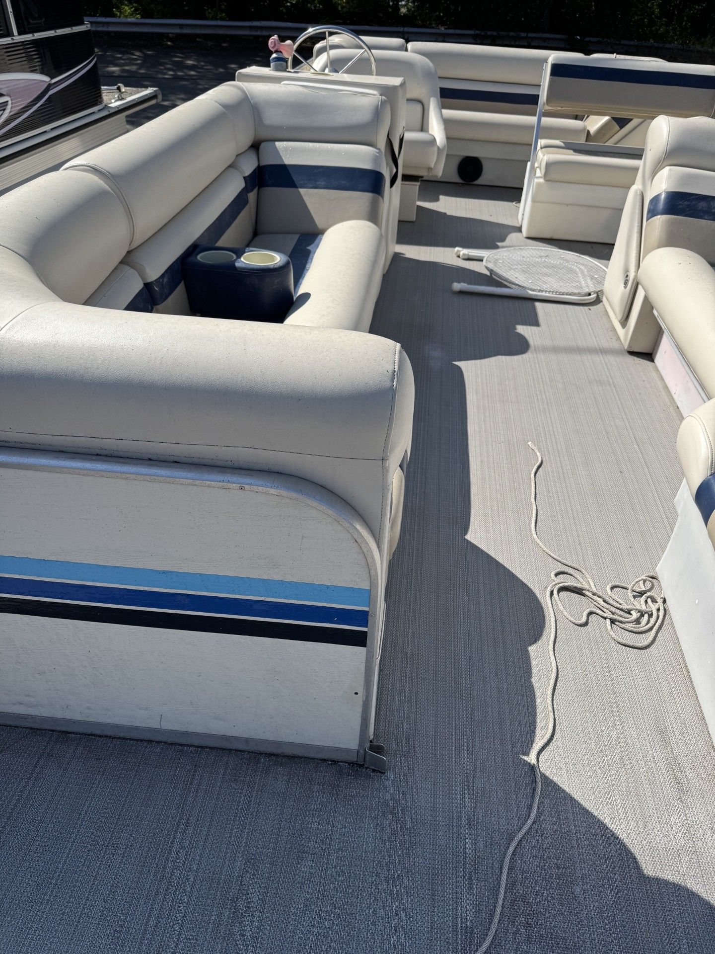 Boat interior with white cushioned seating and gray carpet on a sunny deck