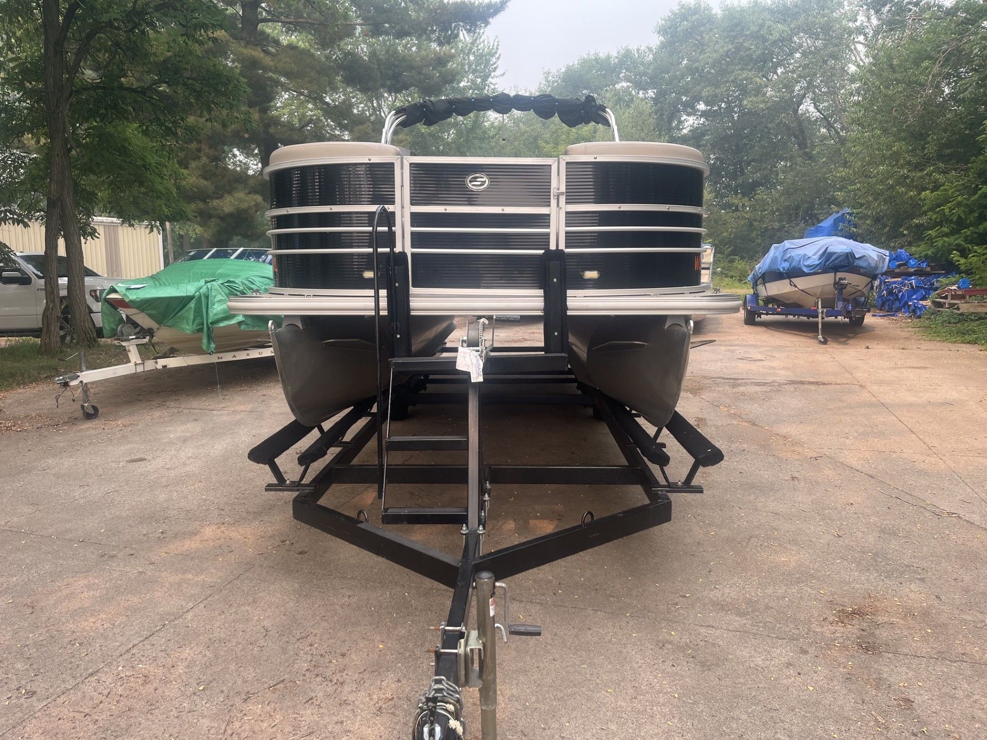 Front view of a black and silver boat on a trailer in a wooded outdoor lot