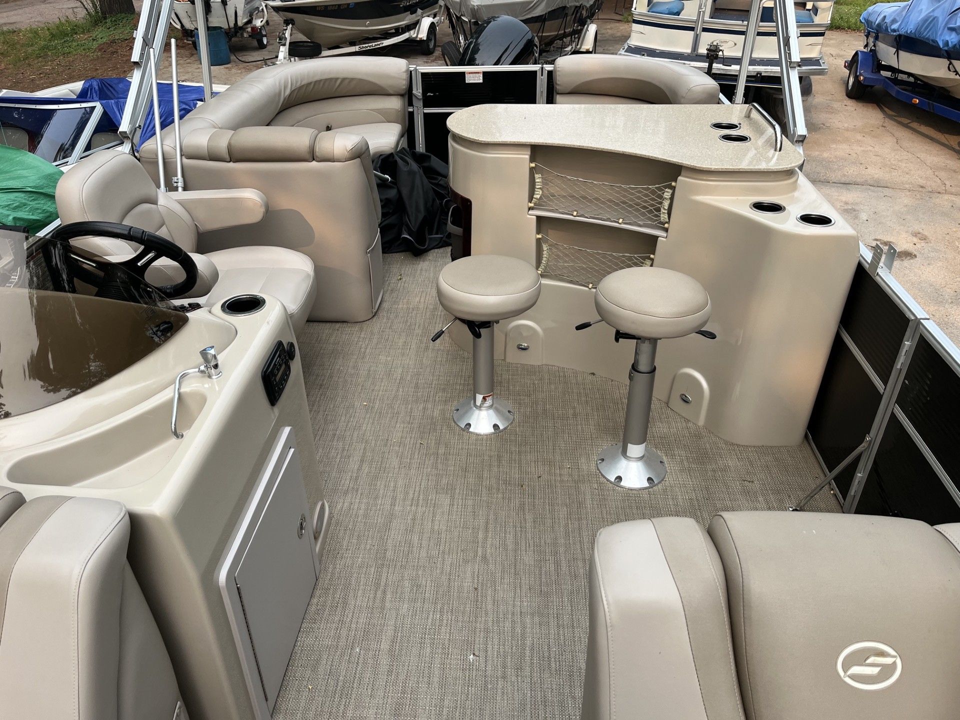 Boat deck with tan seating, two swivel stools, carpeted floor, and helm area in a marina setting