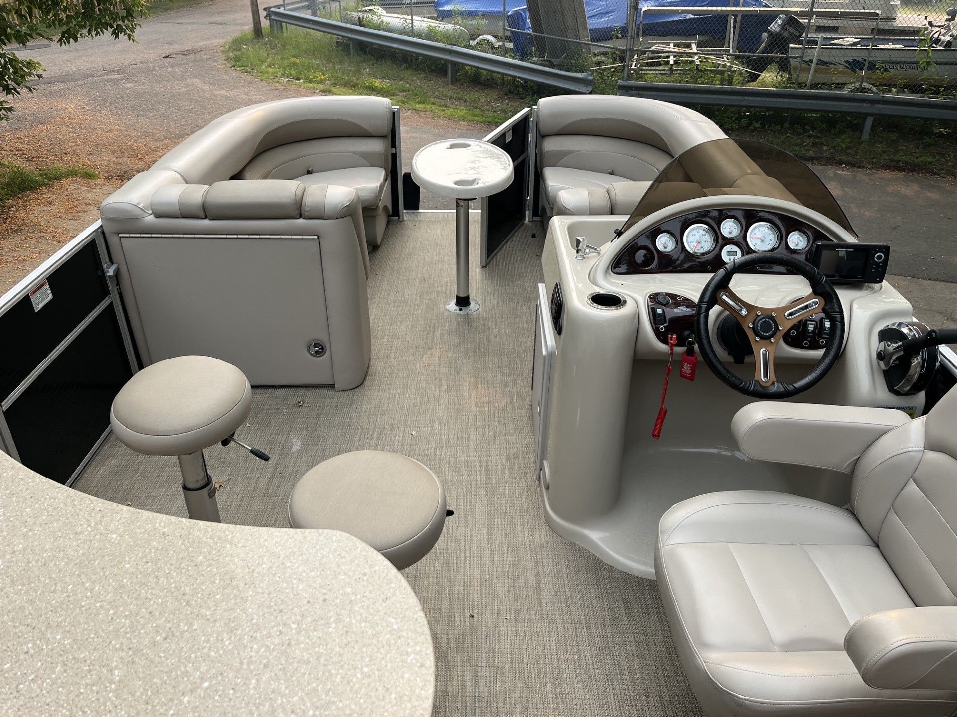 Starcraft 236 Party Lounger boat interior with white seats, tan carpet, steering console, and small table on a dockside lake.
