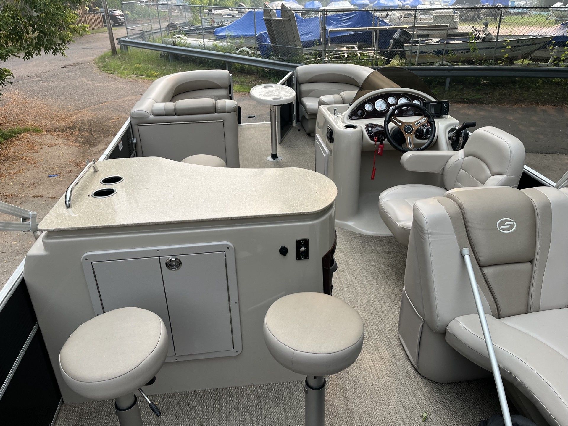 Starcraft 236 Party Lounger boat interior with beige seating, helm, and two round front seats on a gravel shore.