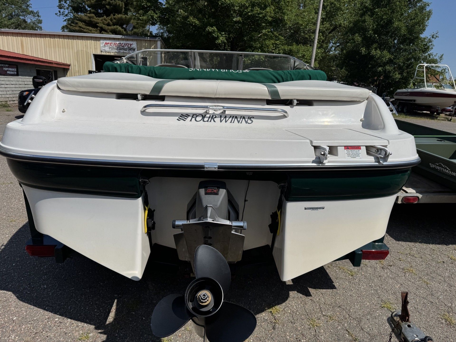 Rear view of a white and green speedboat with open stern panels and outboard motor on a trailer