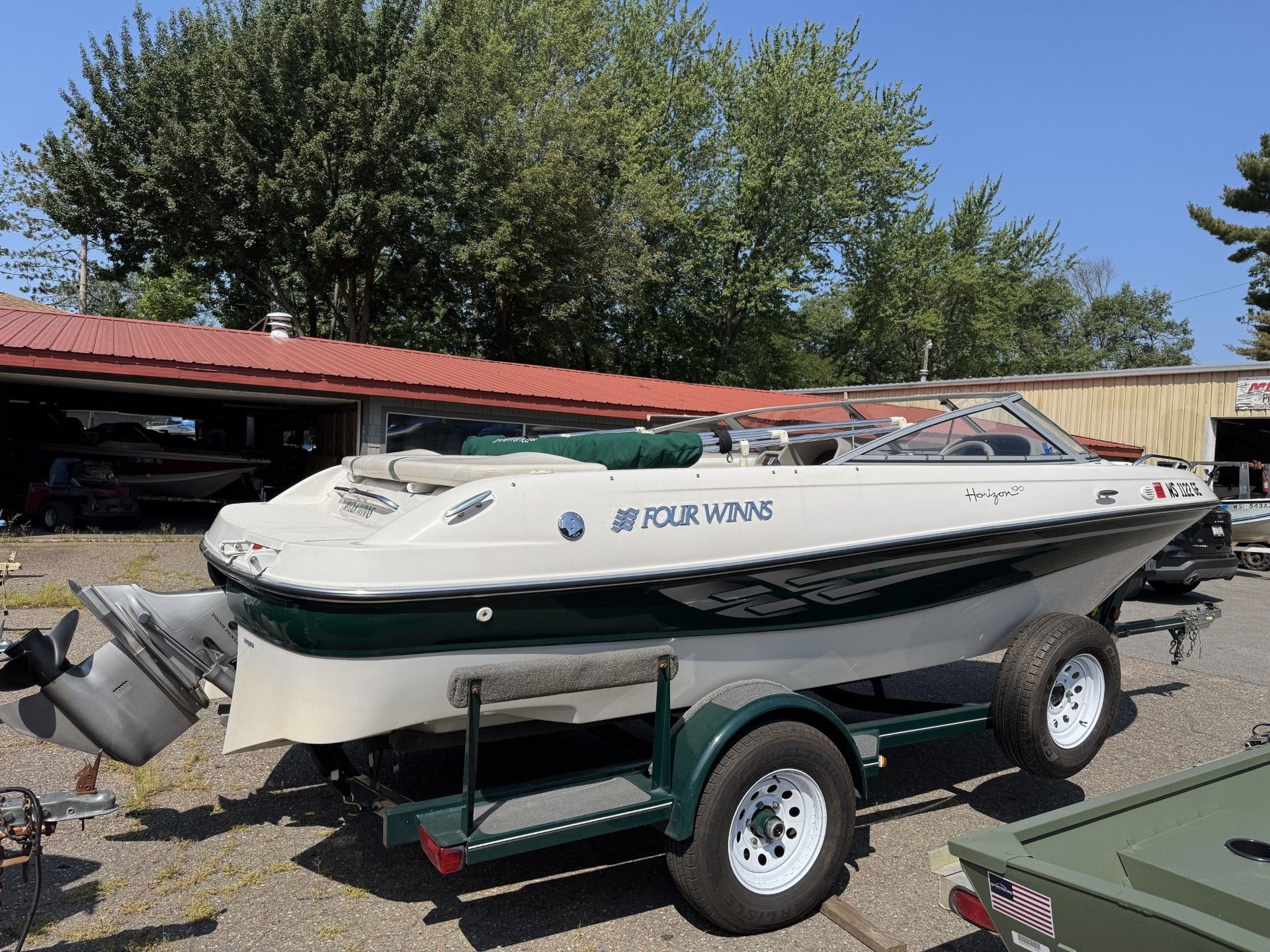 White and blue speedboat on a trailer parked outdoors beside a red-roofed building.
