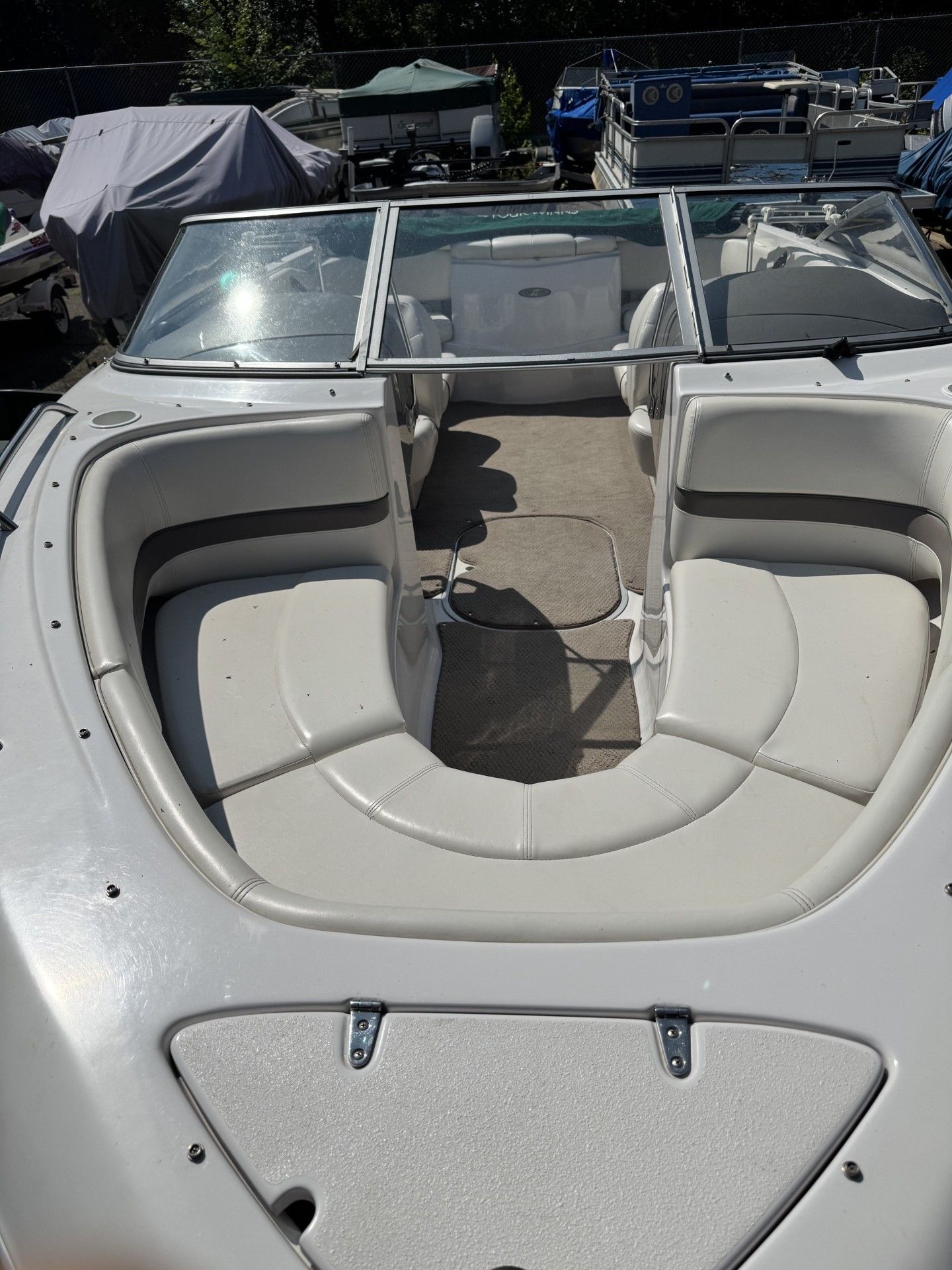 Boat bow seating area with cream cushions and windshield, viewed from the stern.