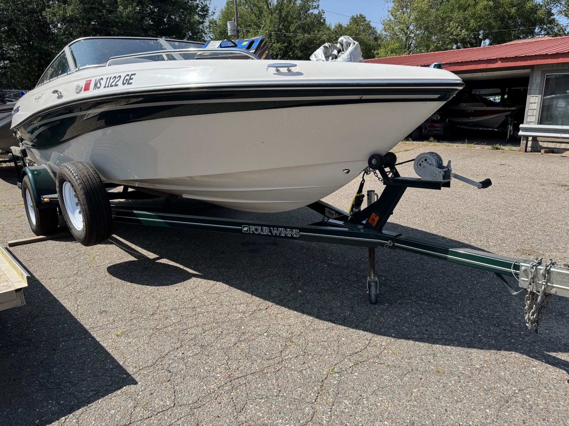White speedboat on a trailer parked in a driveway beside a red-roofed building.
