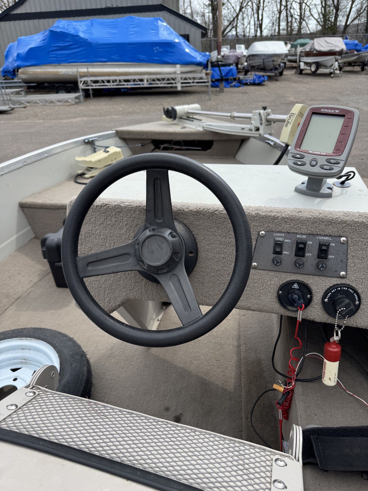 Boat helm with steering wheel, throttle controls, and GPS display in a marina lot