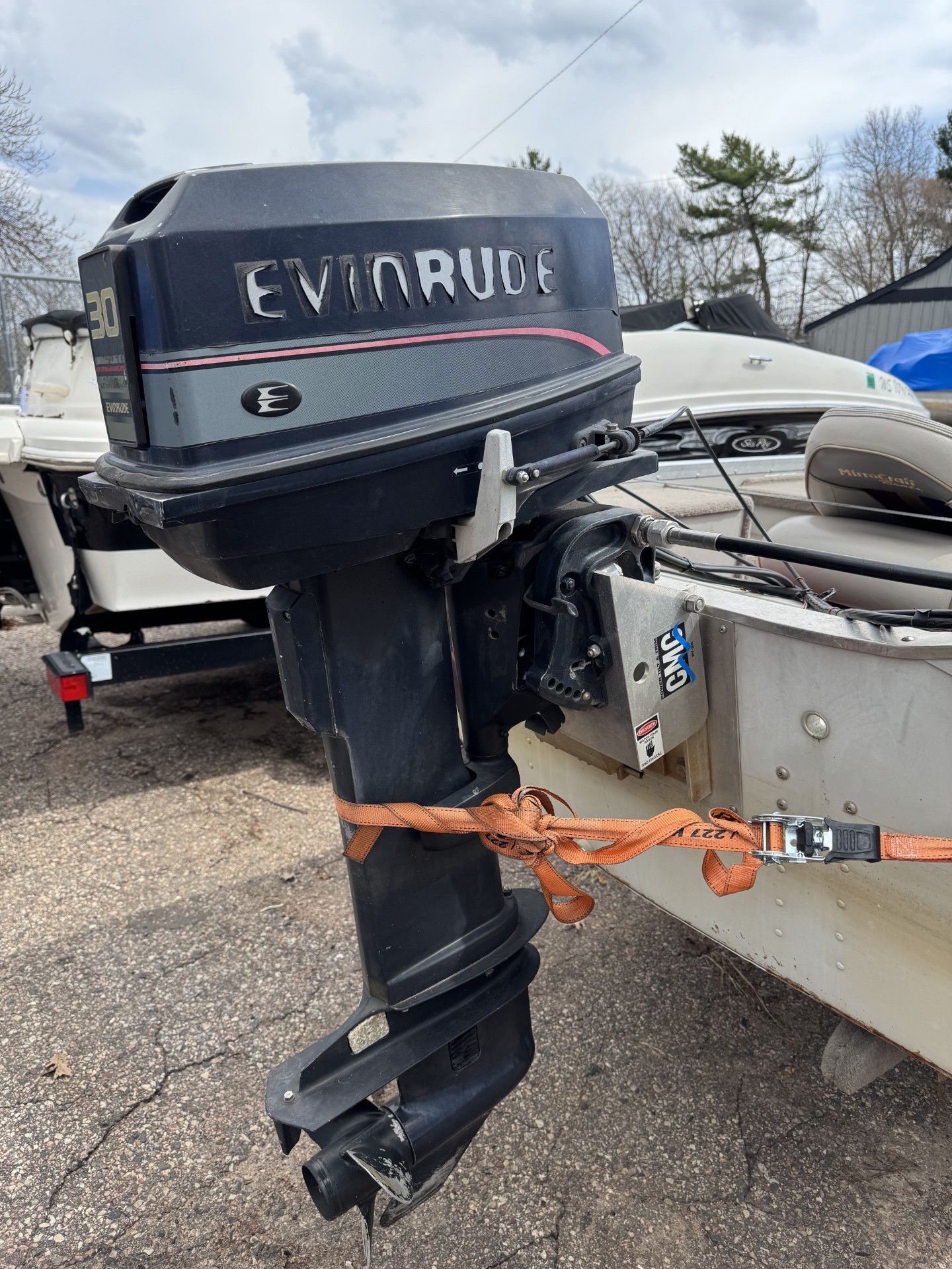 Black Evinrude outboard motor mounted on a boat at a dock, secured with an orange strap.