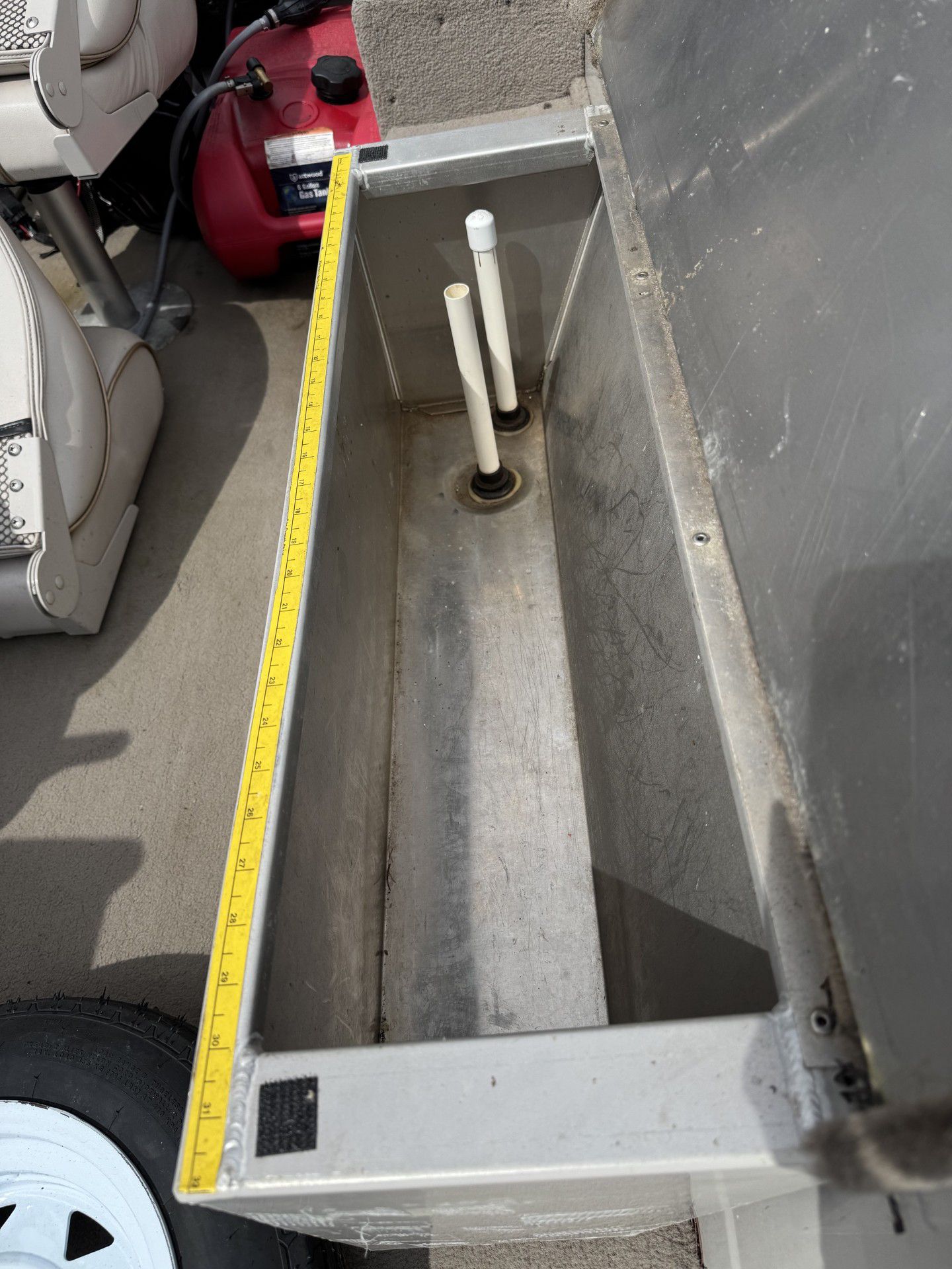 A metal rectangular box with two white pipes inside, measured with a yellow tape in a workshop.