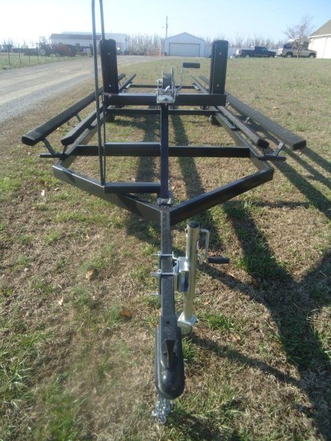 Black trailer with two sets of wheels, designed for transporting long objects.