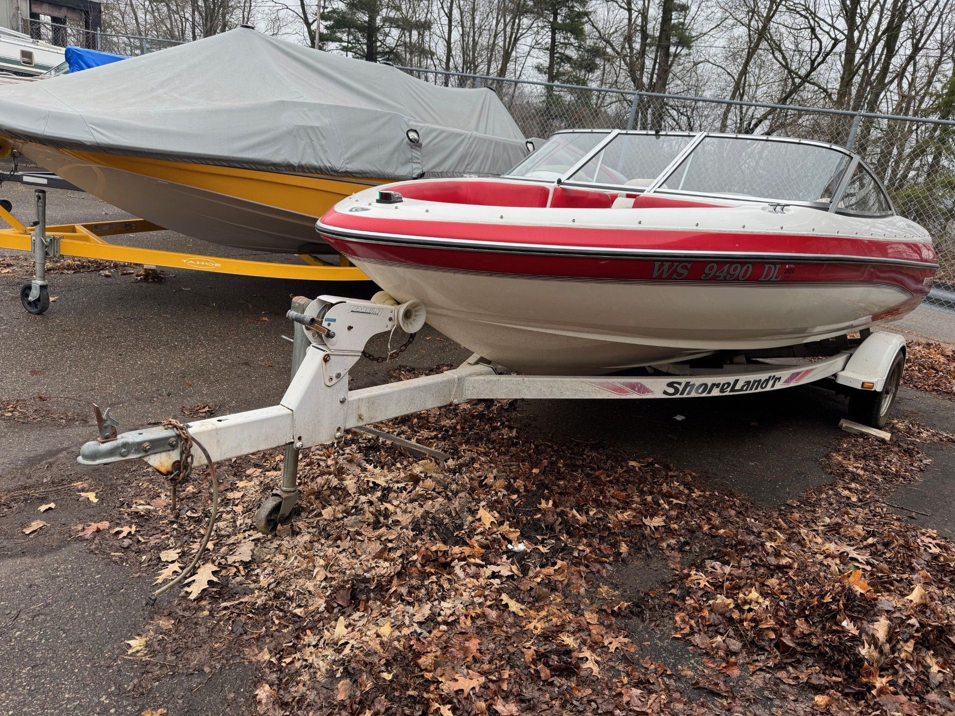 A red and white boat is parked on a trailer next to a yellow boat.
