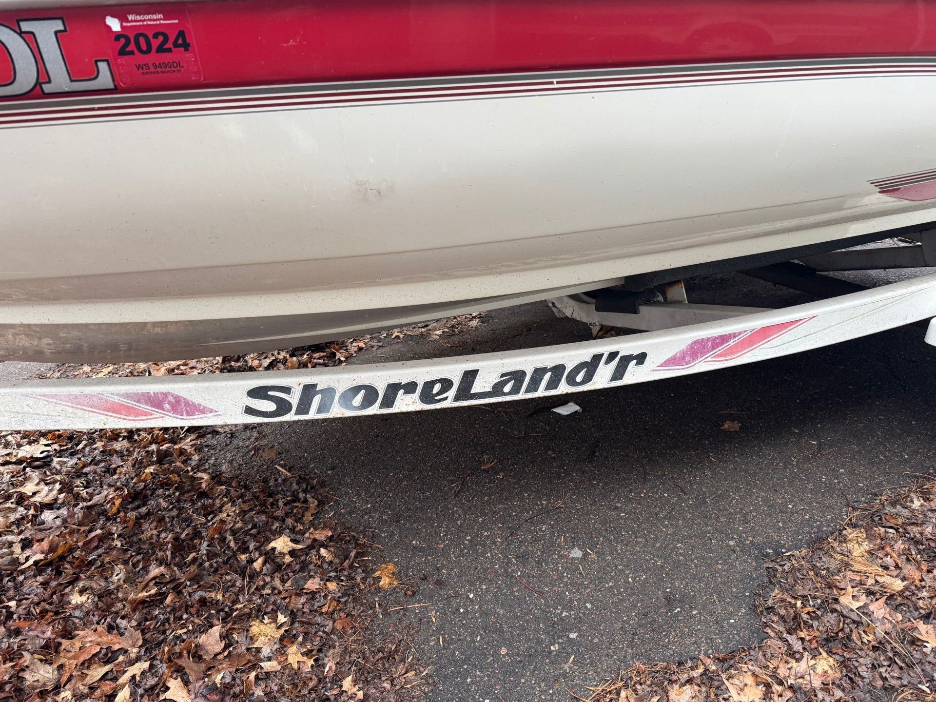 A red and white boat with a trailer attached to it is parked on the side of the road.