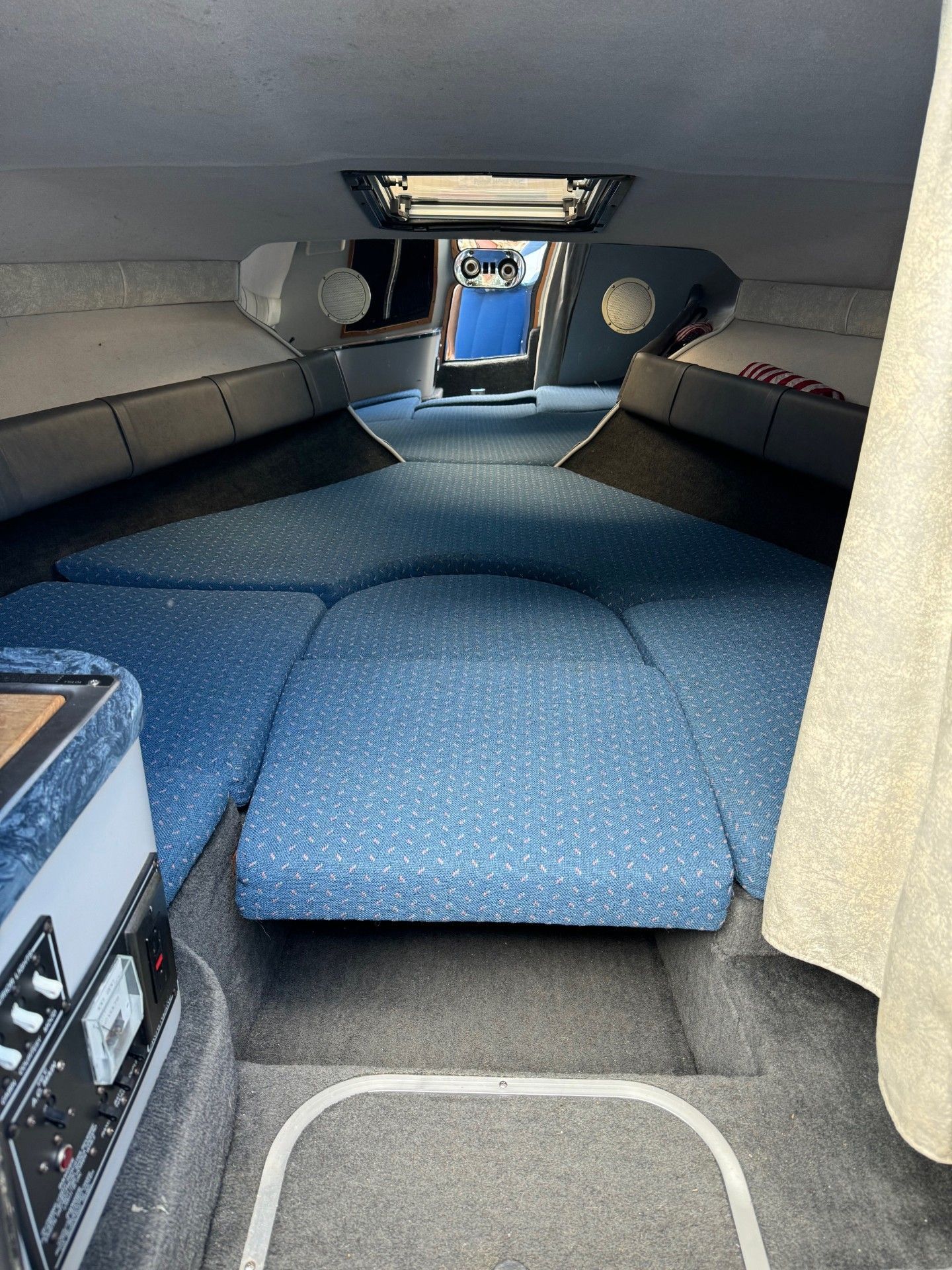 The inside of a boat with blue cushions and a beige curtain