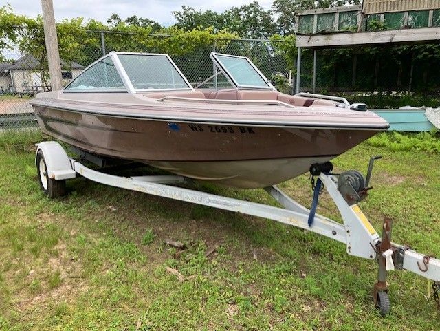 A brown boat is parked on a trailer in the grass.