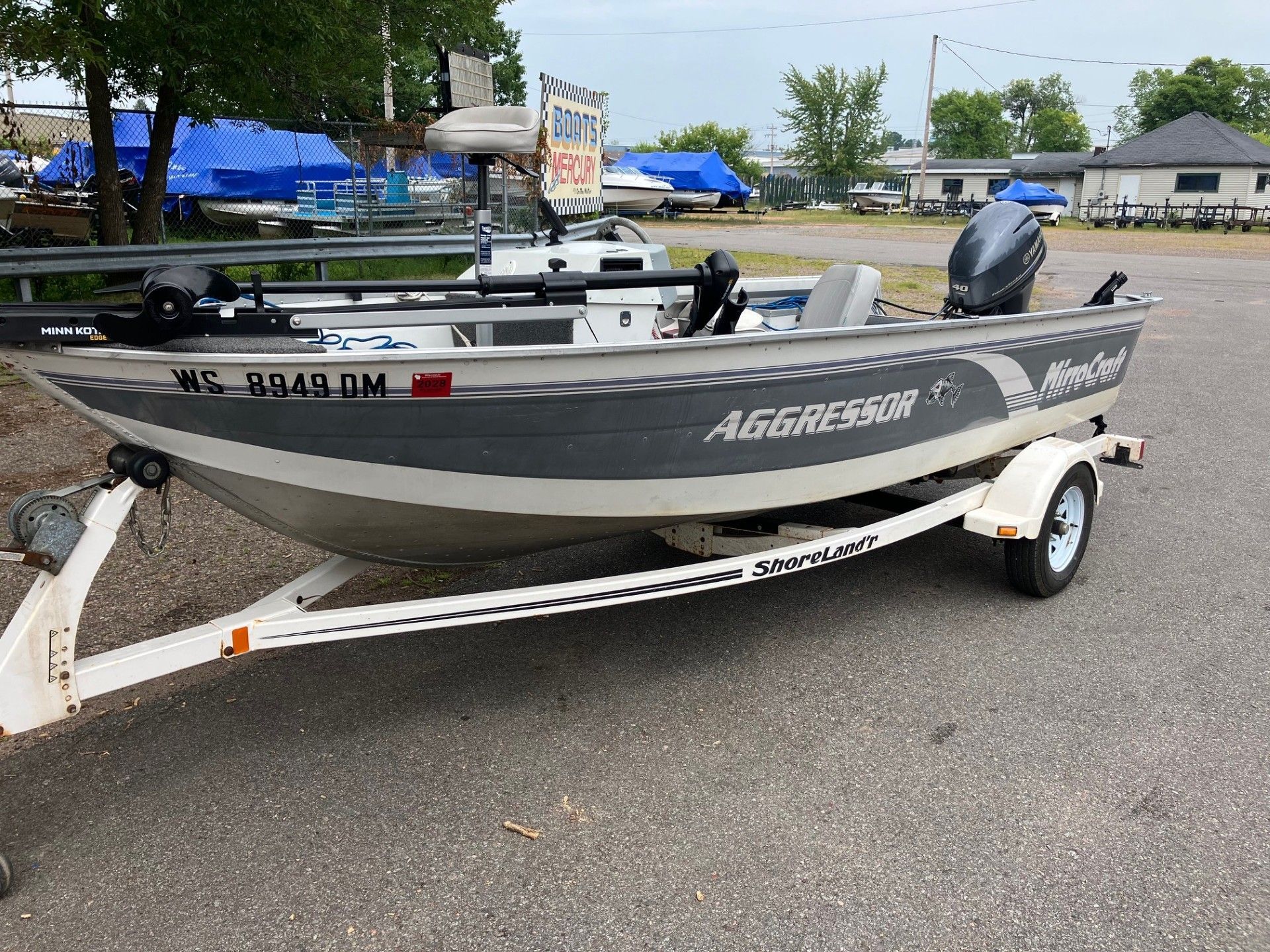Aluminum fishing boat on a white trailer parked on pavement. The boat has a dark gray hull with 