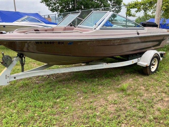 A boat is parked on a trailer in the grass.